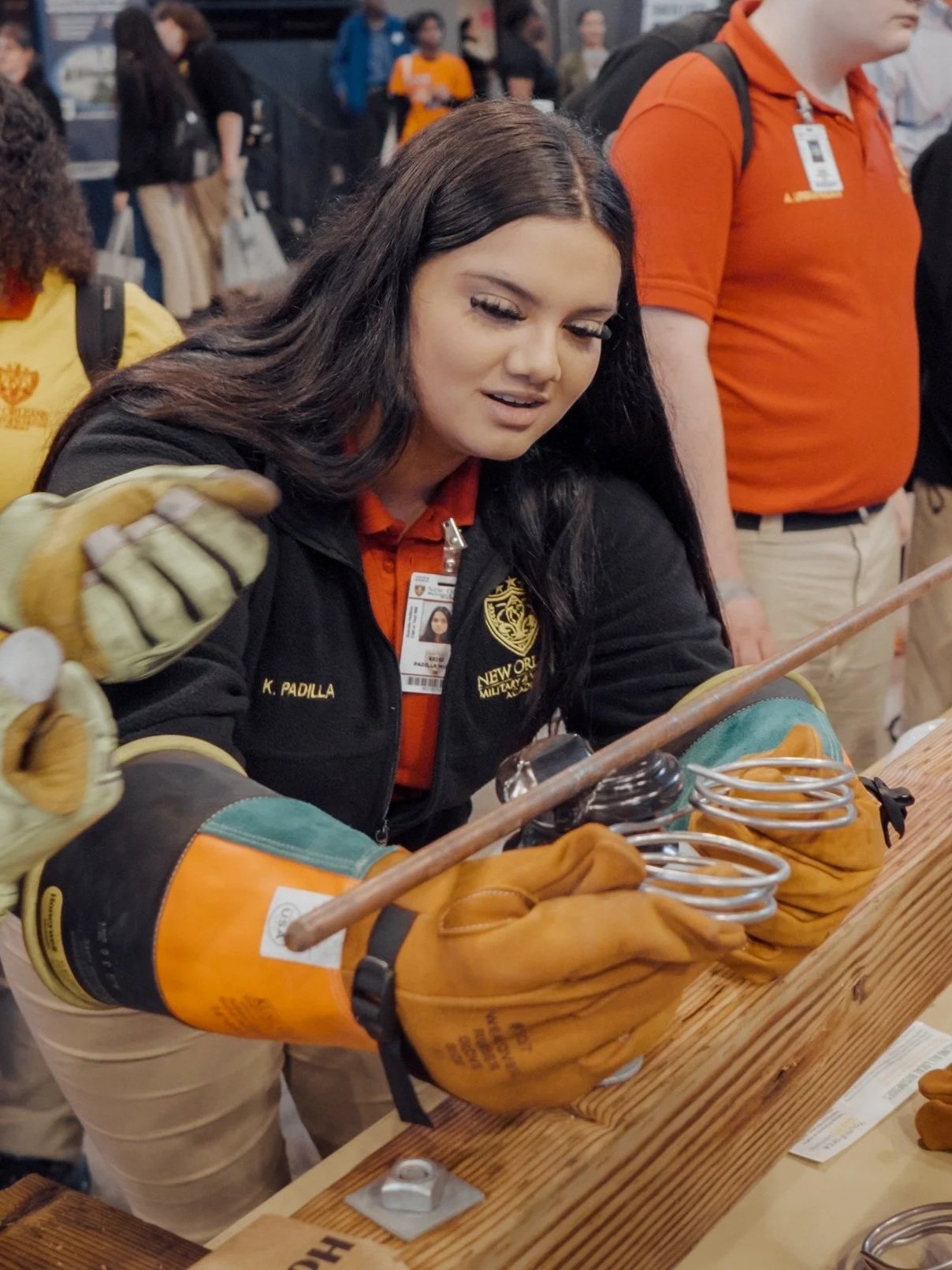 A girl in a black sweater and thick tan work gloves handles two metal coils underneath a metal rod.