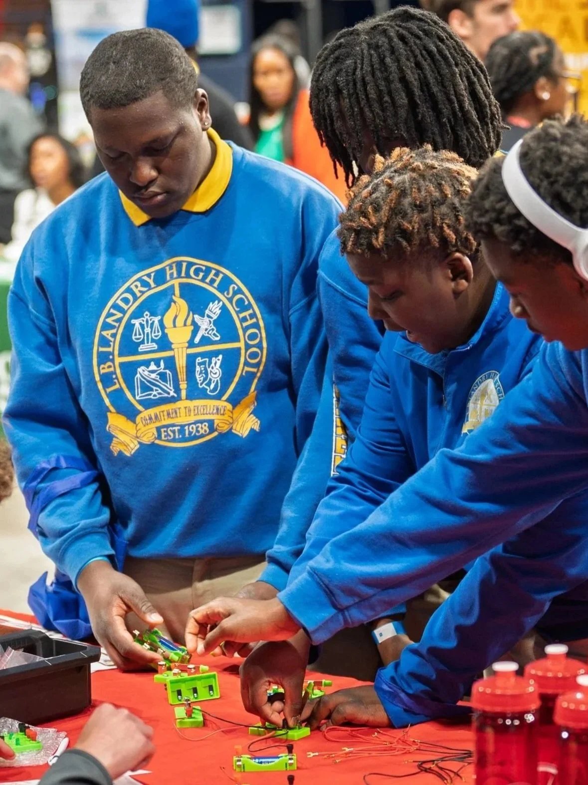 Students in bright blue L.B. Landry High School shirts stand around a table playing with circuit boards.