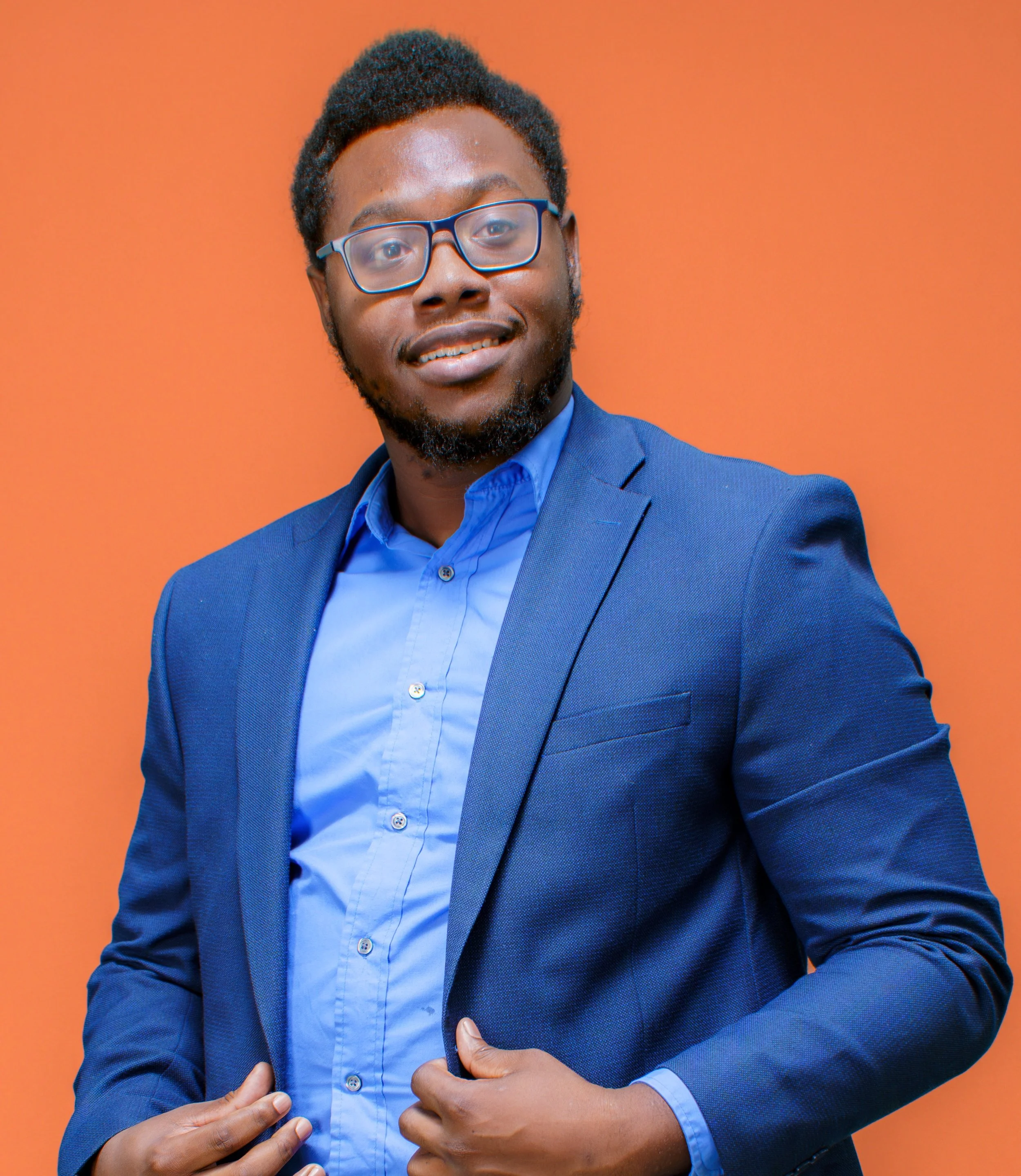 Photo of James Milligan III, a YouthForce NOLA Intern alumni. James stands against an orange background and is wearing a blue suit.