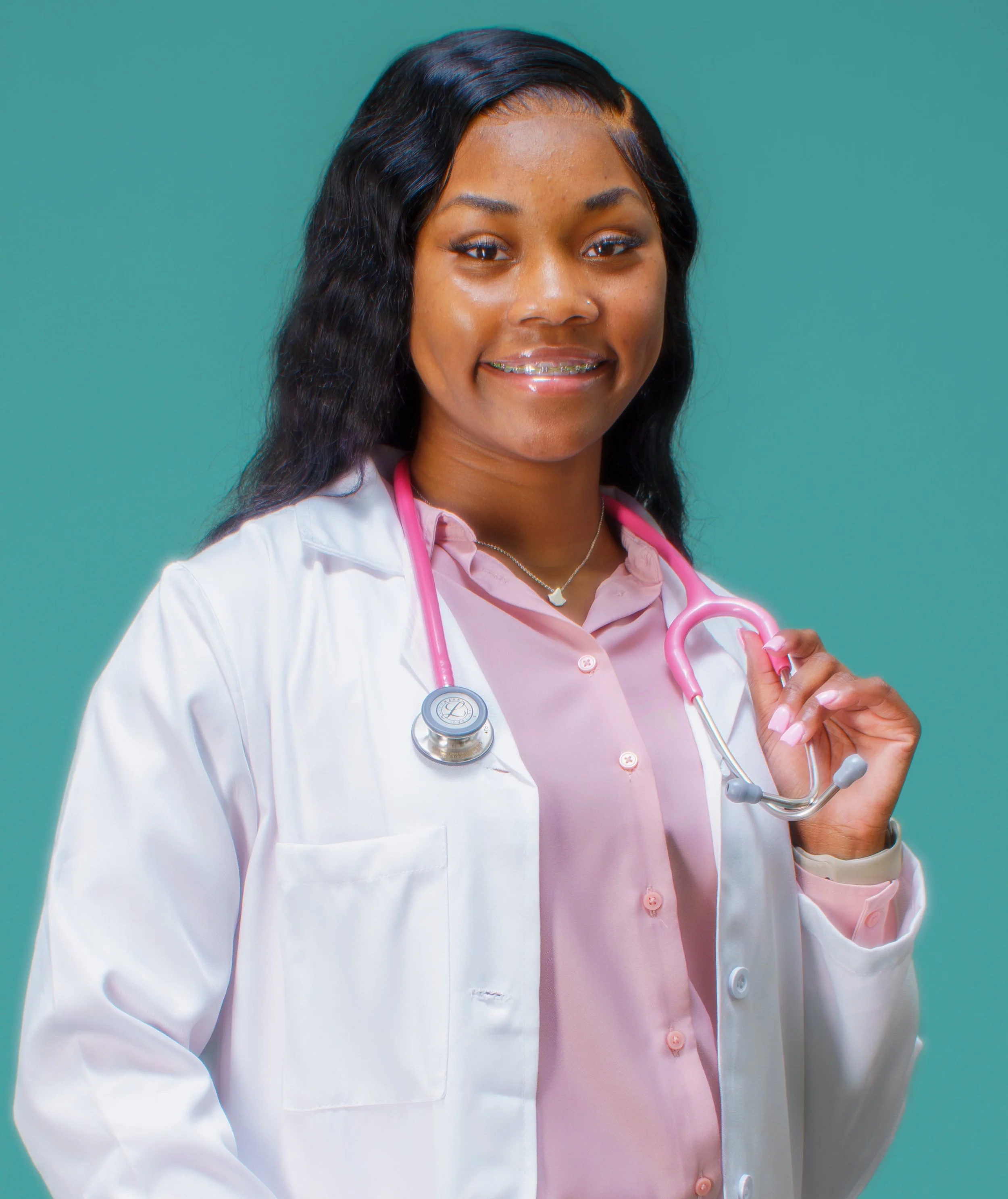 Photo of Psalms Joseph, a YouthForce NOLA Intern alumni. Psalms is standing against a blue background and is wearing a white lab coat over a pink button up shirt.