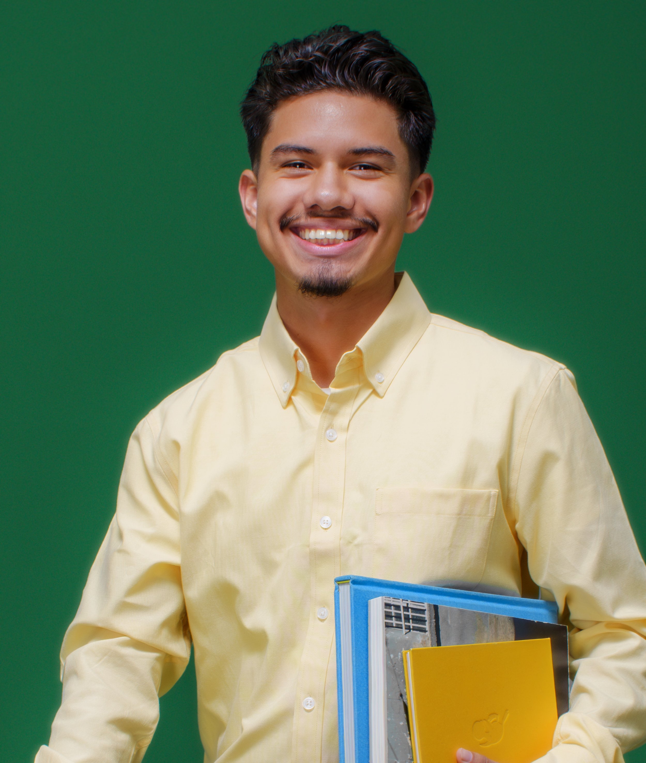 Photo of Dylan Lazo, a YouthForce NOLA Intern alumni. Dylan stands against a dark green background and is wearing a yellow button up shirt.