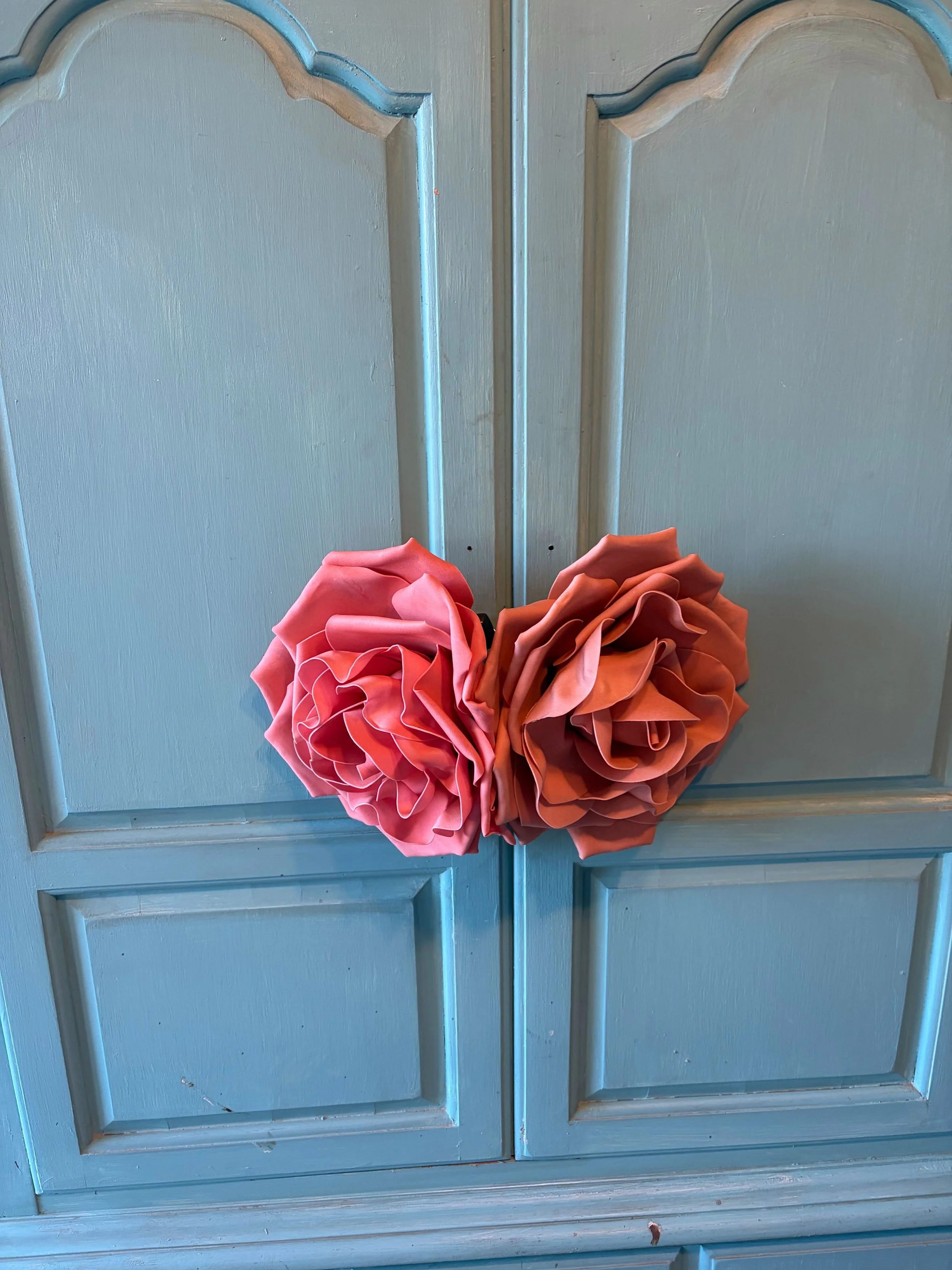 A blue wooden door with decorative panels, decorated with a bouquet of large pink and orange paper flowers.