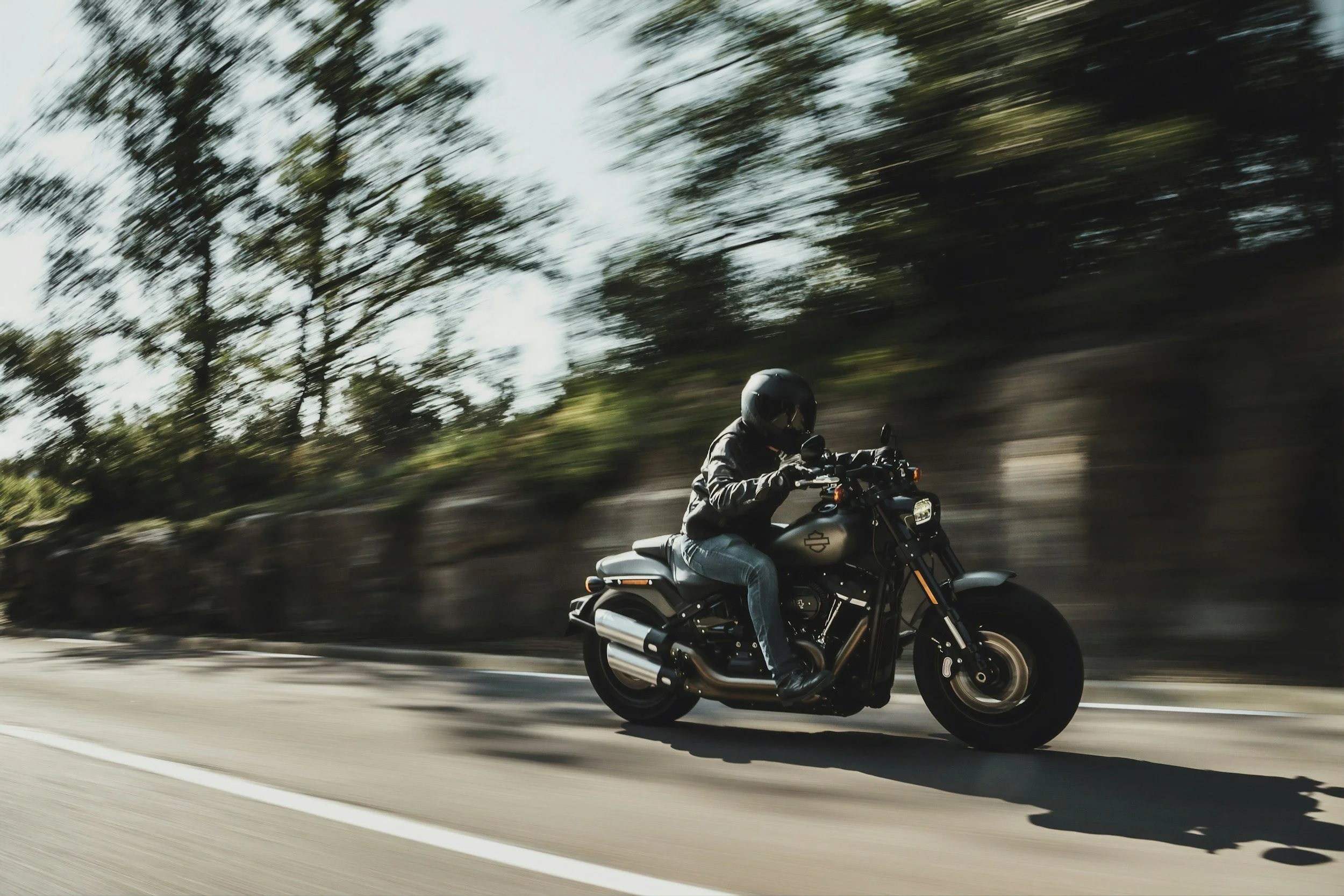A person wearing a helmet riding a black motorcycle on a highway with trees in the background.