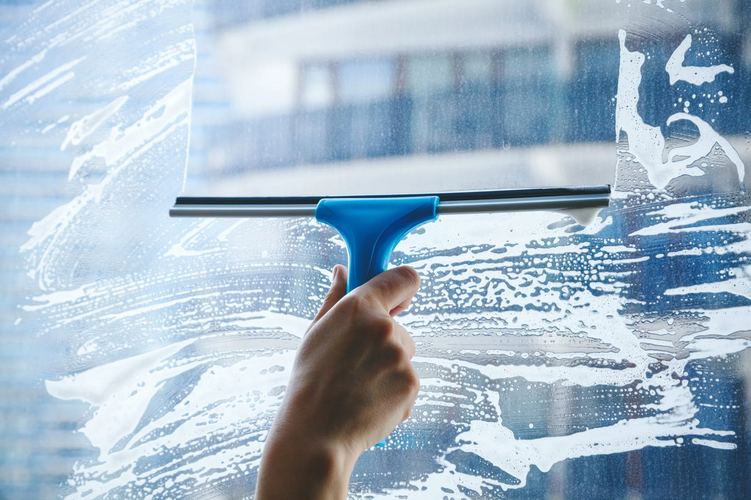 A person using a squeegee to clean a glass window with soap and water.