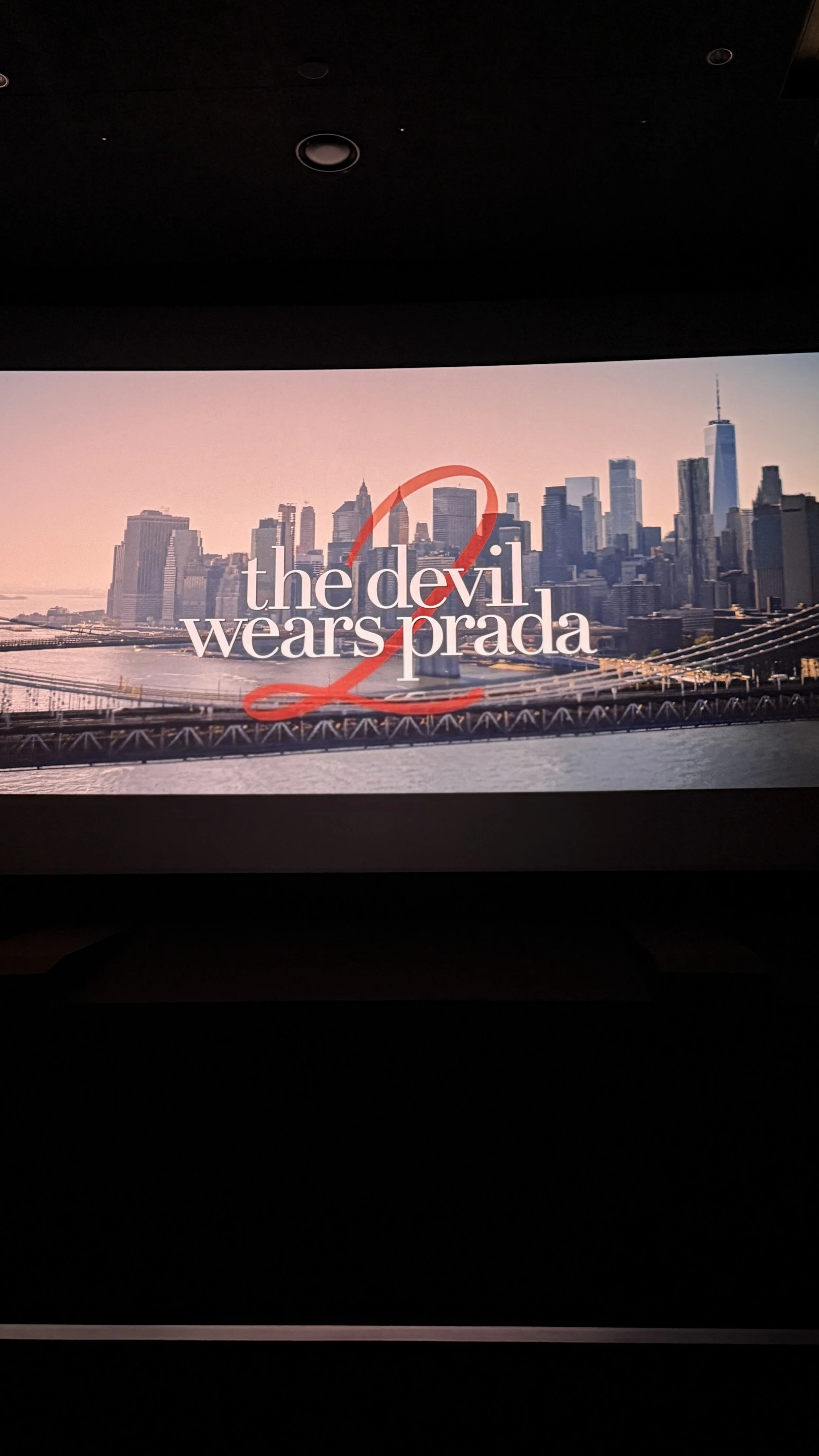 뉴욕시 스카이라인과 브루클린 다리 모습이 보이고, 'the devil wears prada'라는 문구가 적혀 있는 디지털 화면