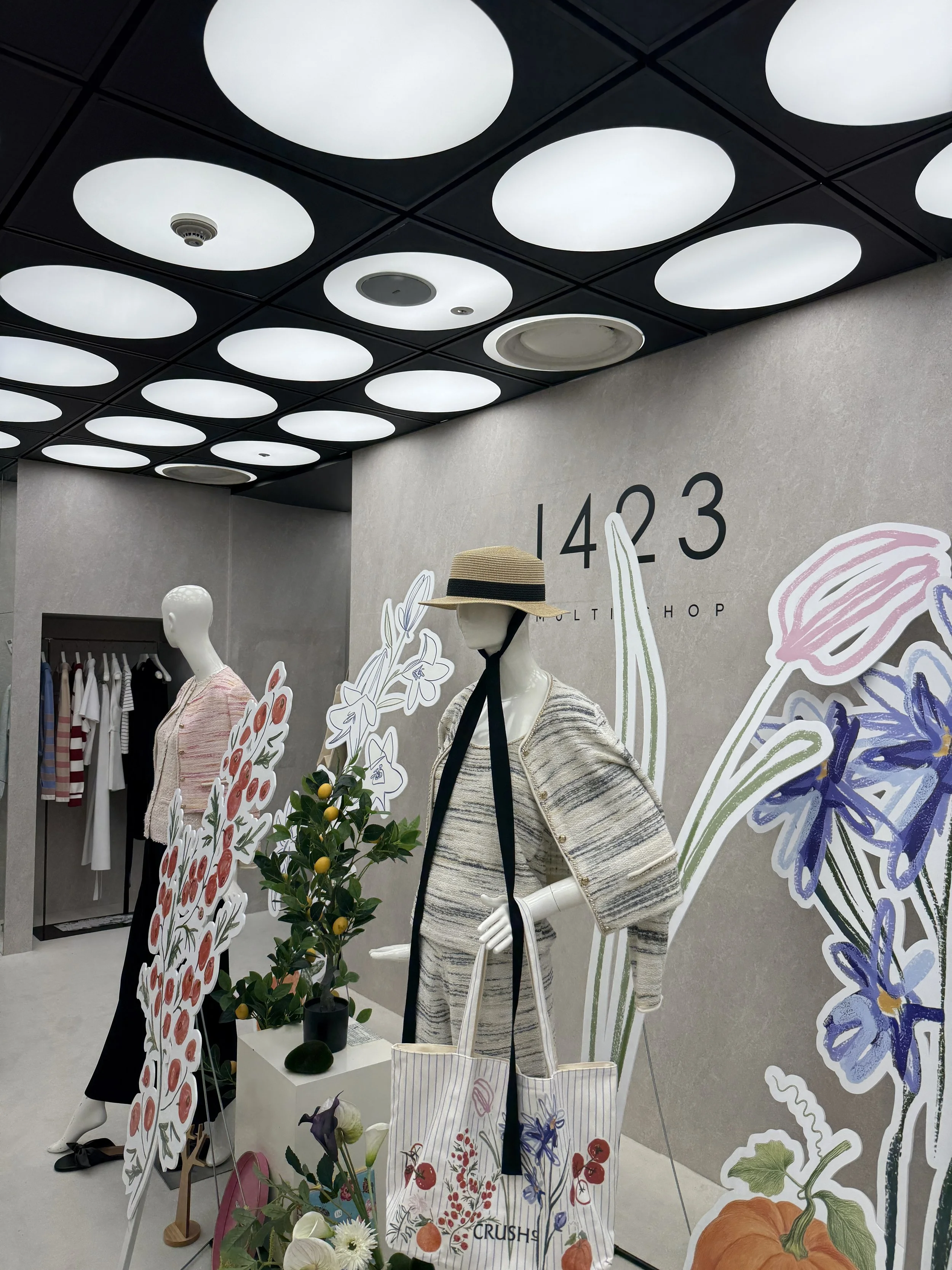 가게 내부 전경, 남성용 옷과 가방이 전시된 매장, 벽에 숫자 1423과 식물 그림 장식이 있음, mannequin이 모자와 가방을 착용하고 있음.