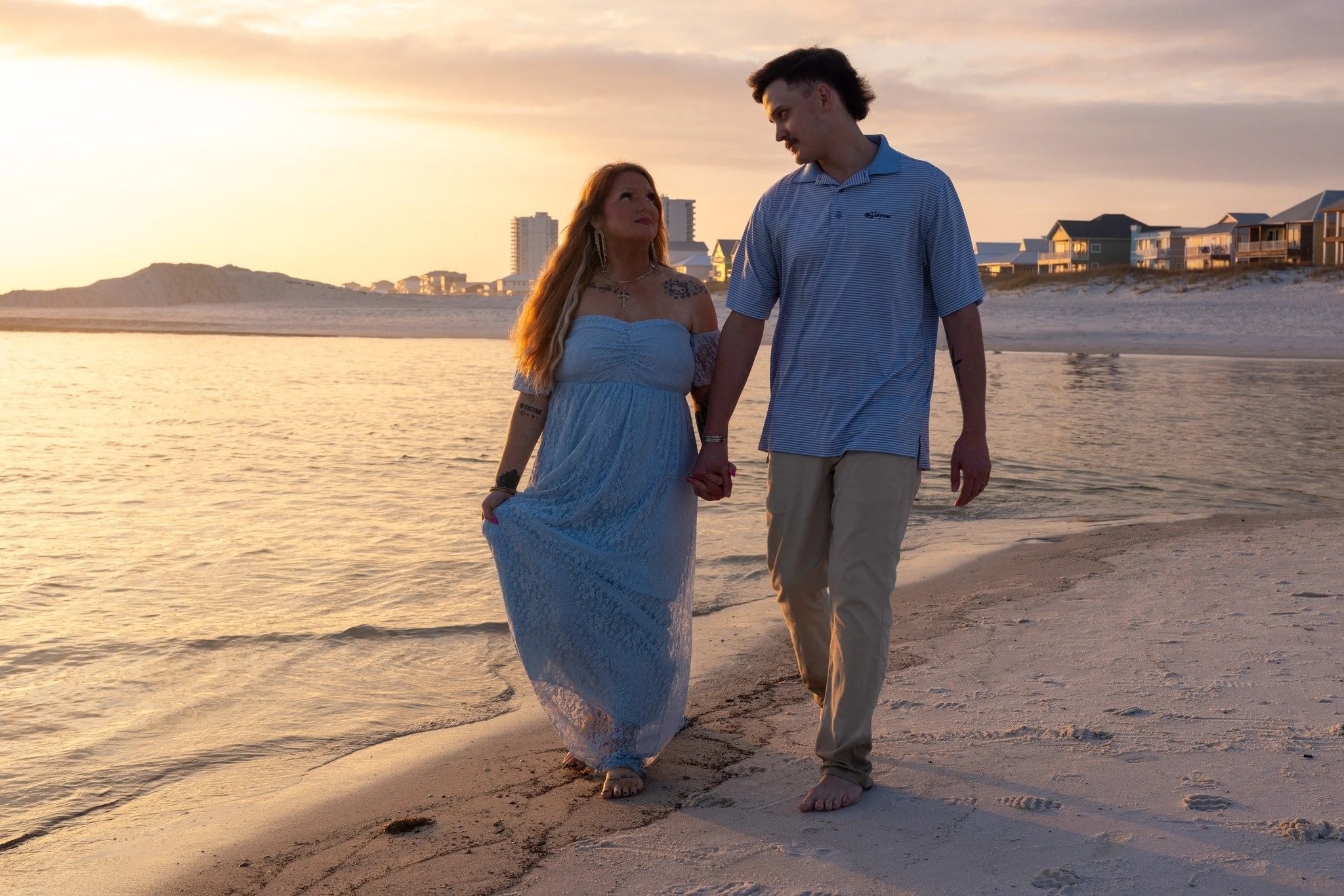 A couple holding hands, walking on the beach during sunset, with condos in the background.