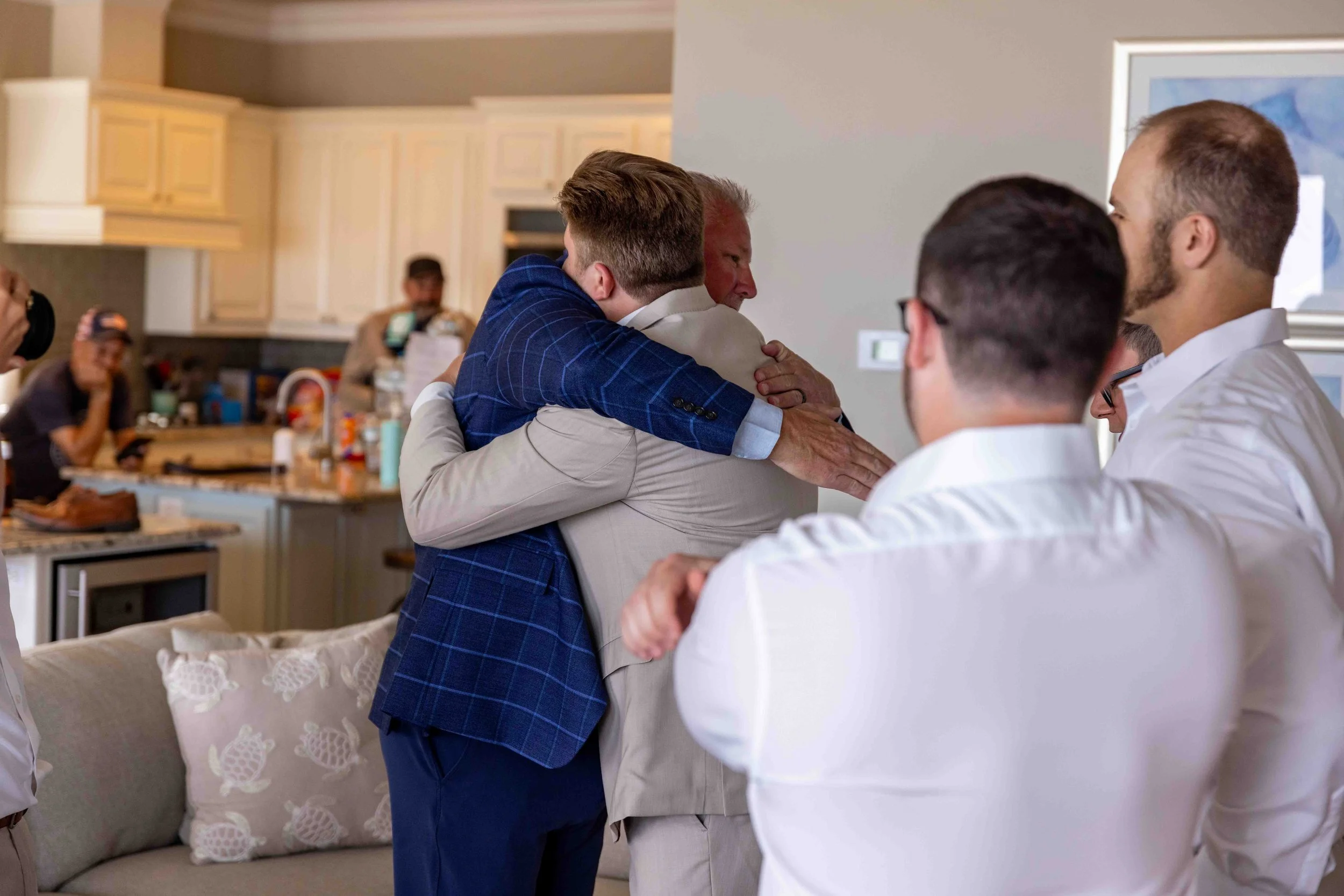 Several men embracing in a kitchen during a social gathering.