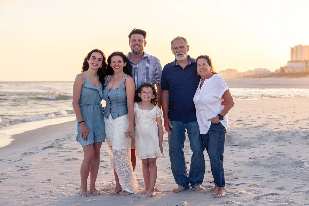 A group of six people, including three women, two men, and a girl, standing on a beach during sunset