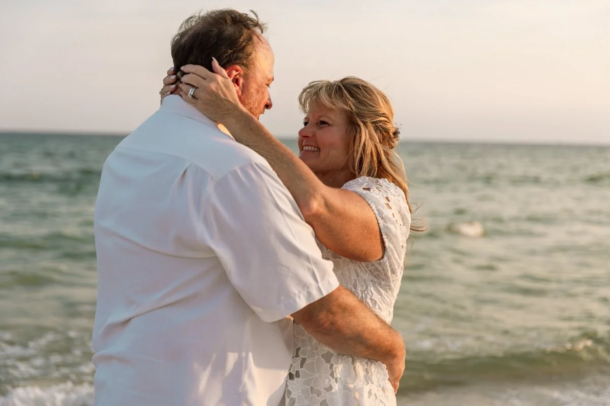 A smiling couple is embracing on the beach near the ocean during sunset.