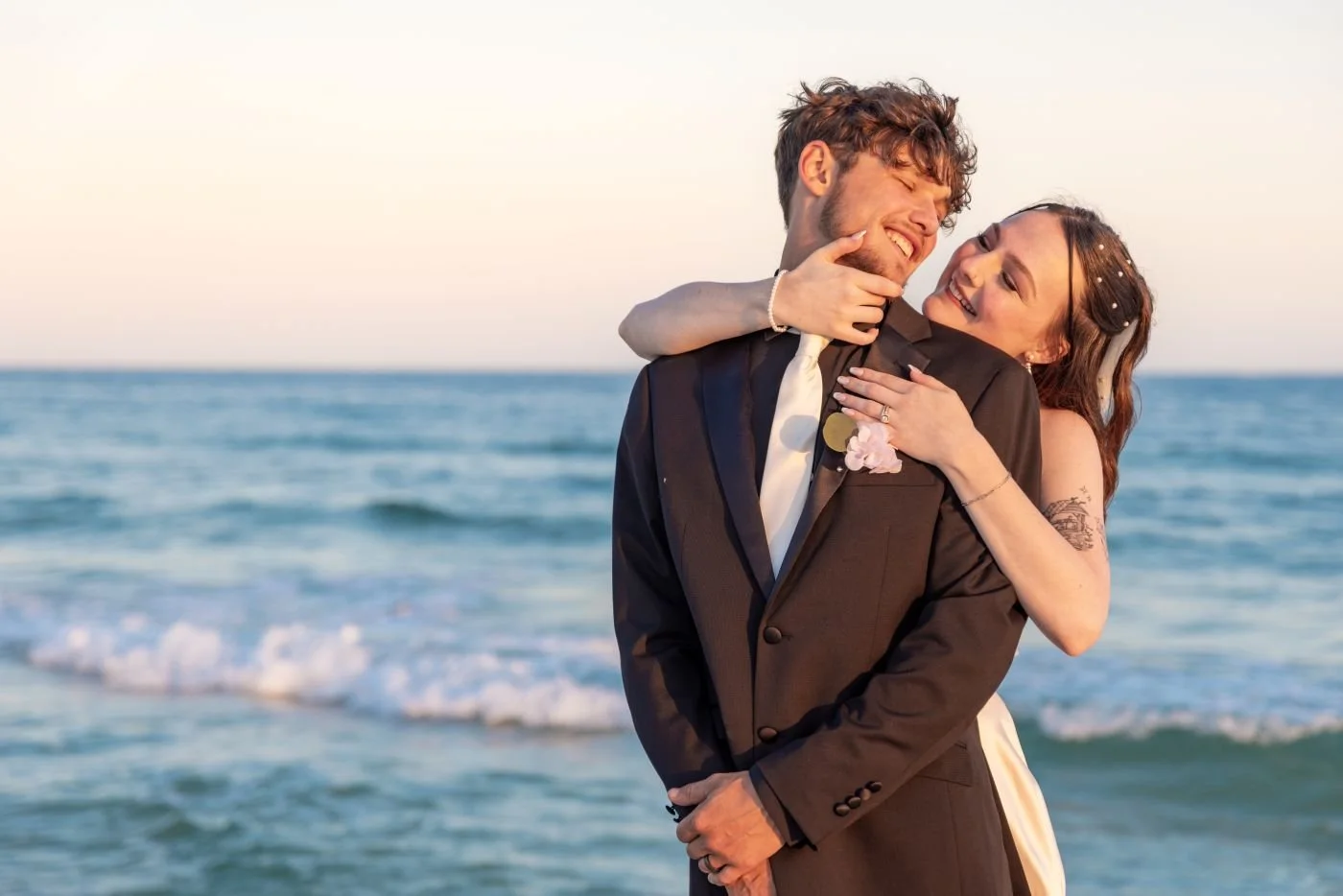 A bride hugging the groom from behind standing on the beach, Wedding photography done by Kyle Rossi