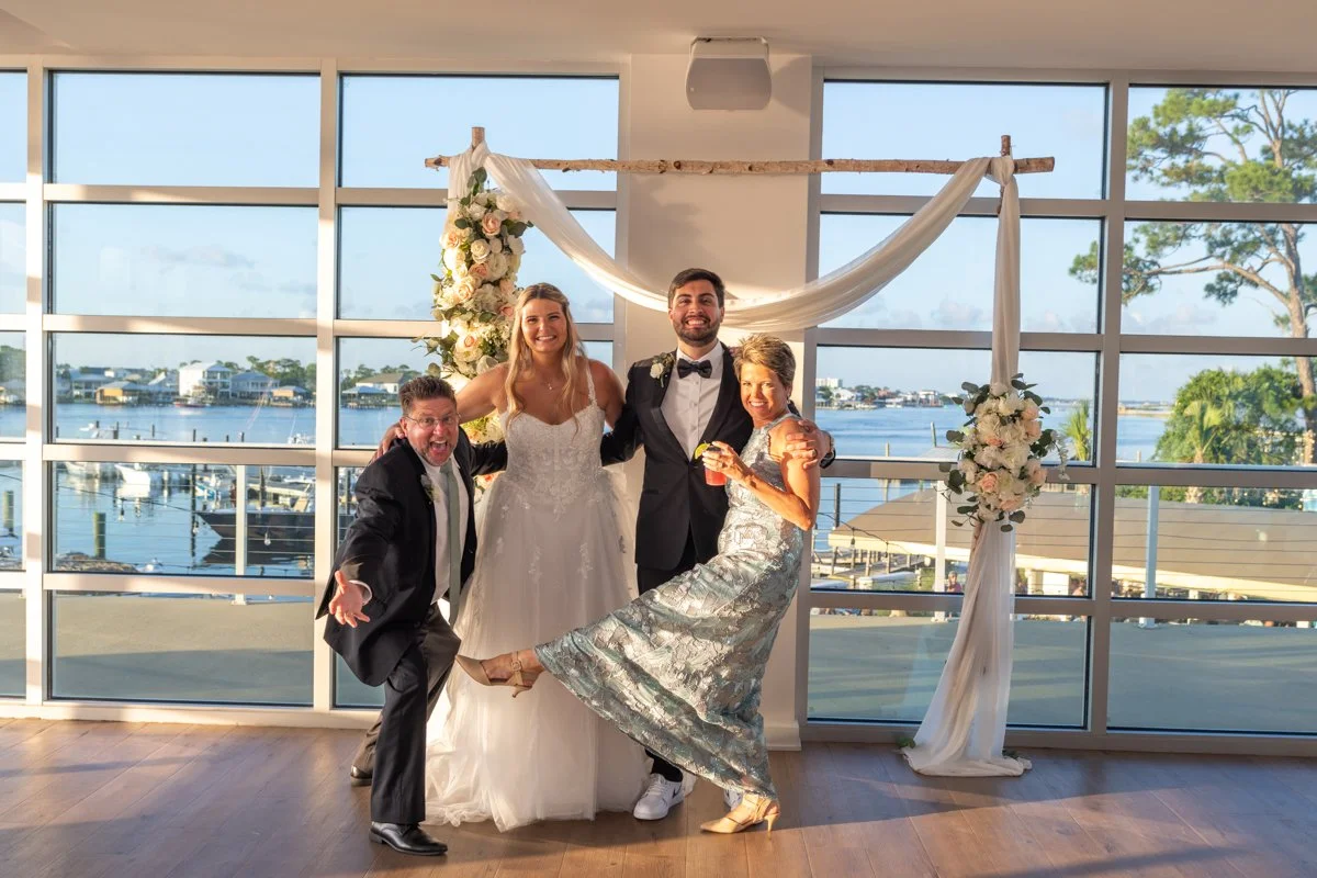 People celebrating at a wedding reception with a waterfront view and a floral wedding arch.