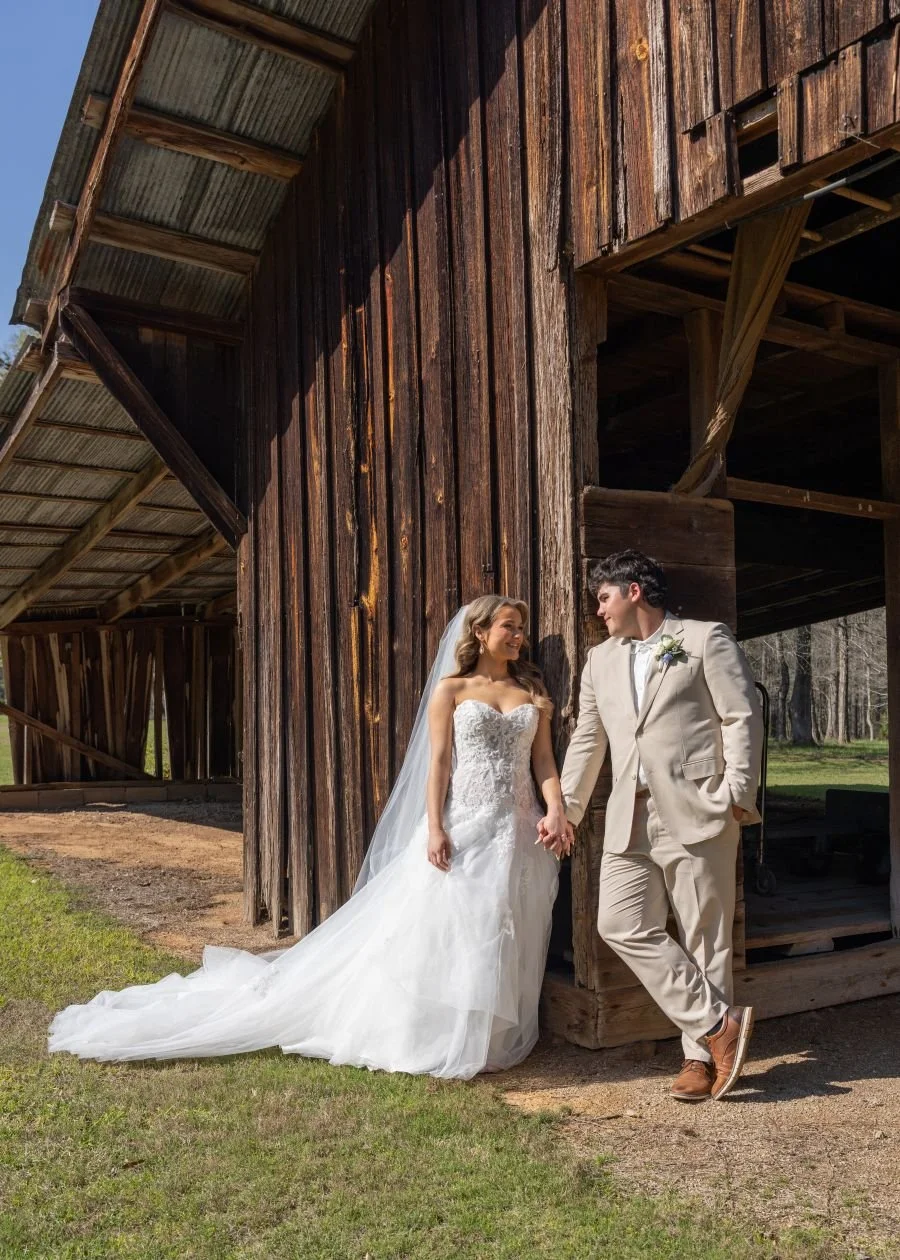 Bride and groom holding hands leaning against an old barn doorway looking at each other. Gulf Shores Wedding Photography