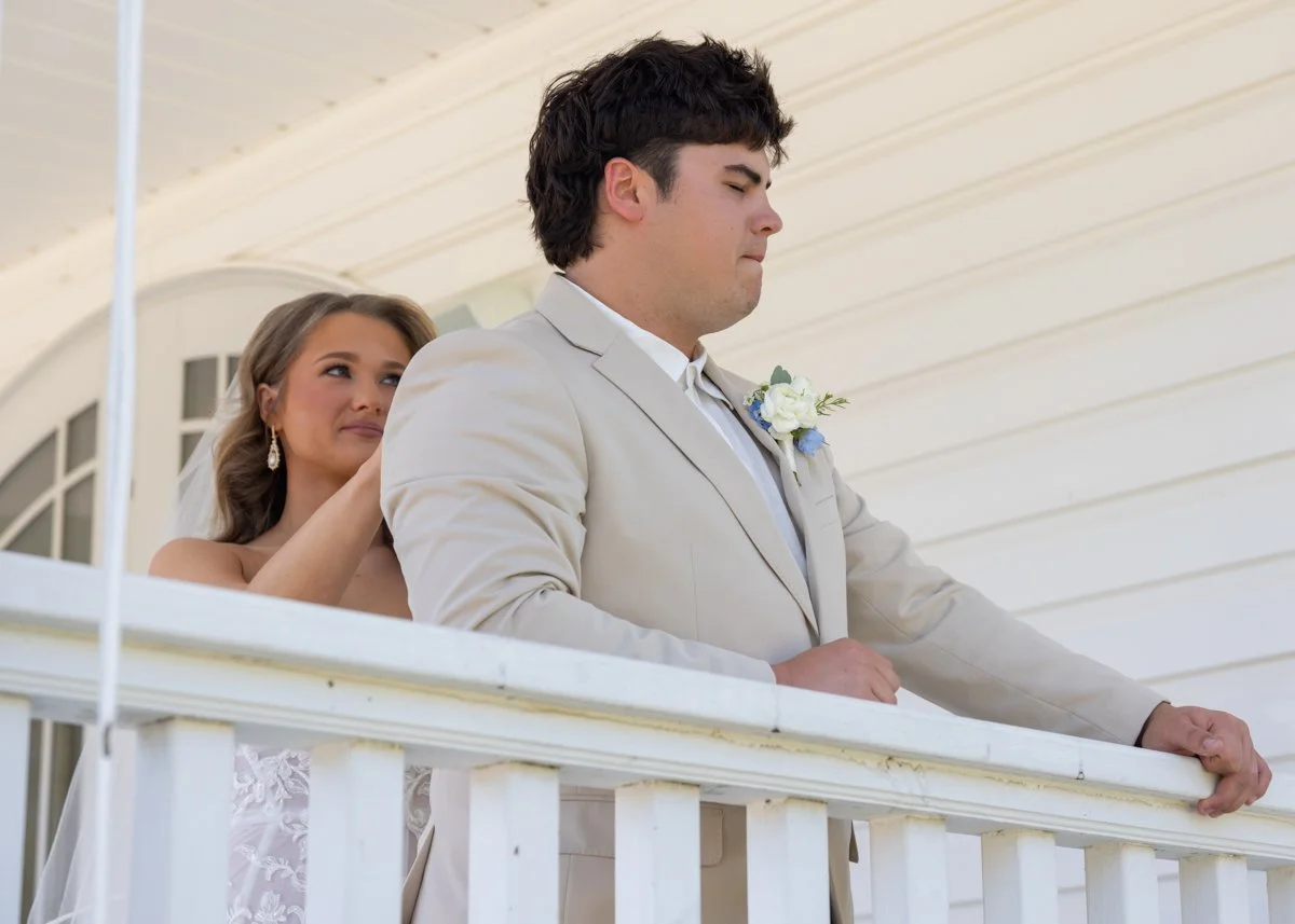 A bride and groom on a porch during a wedding ceremony, with the bride looking at the groom and the groom looking ahead, holding the porch railing.
