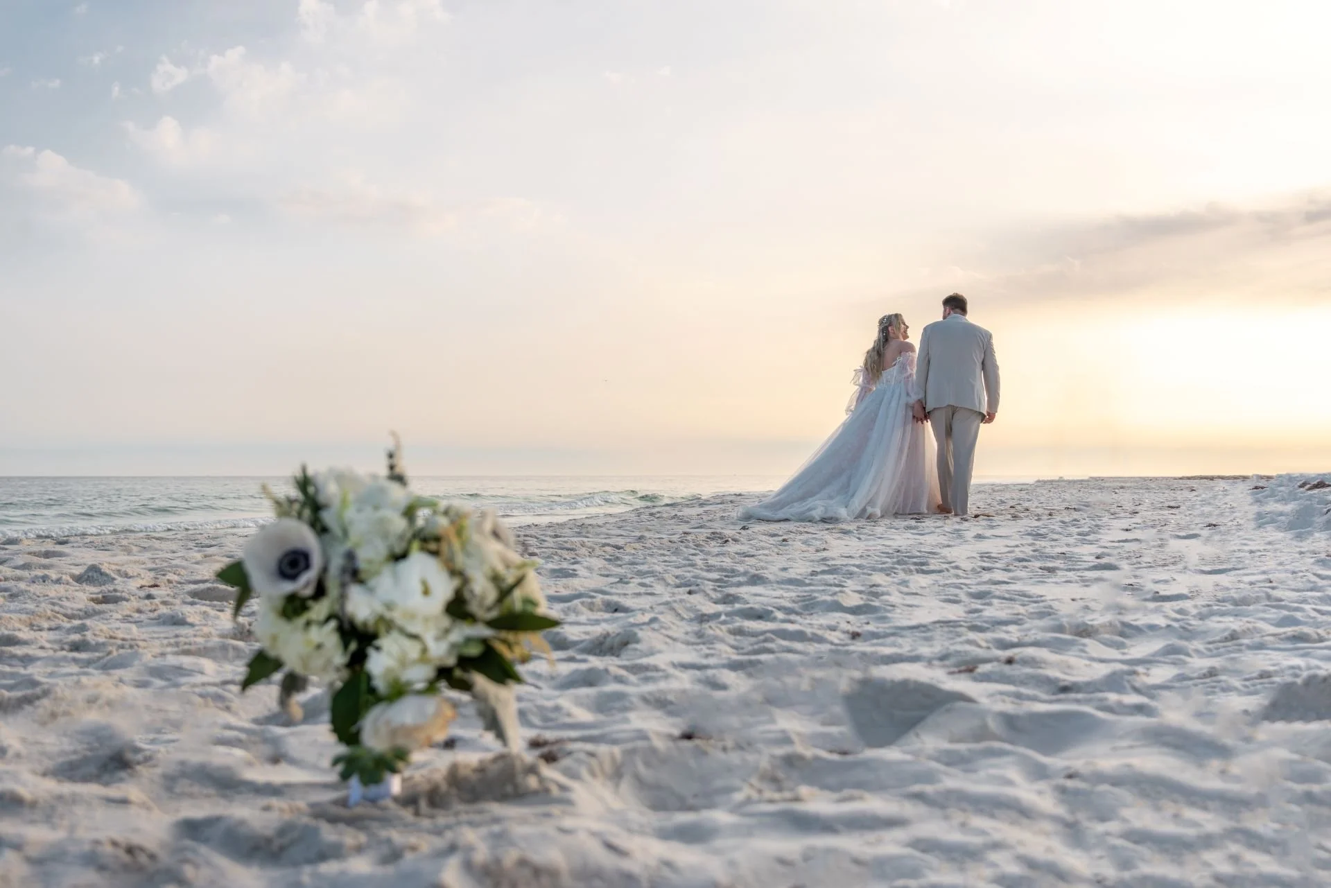 Bride and groom holding hands walking on the beach towards the sunset. Gulf Shores wedding photographer