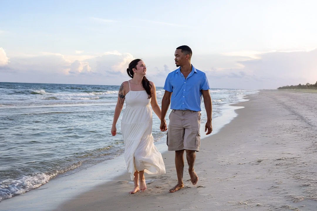 A couple holding hands and walking along the beach at sunset.