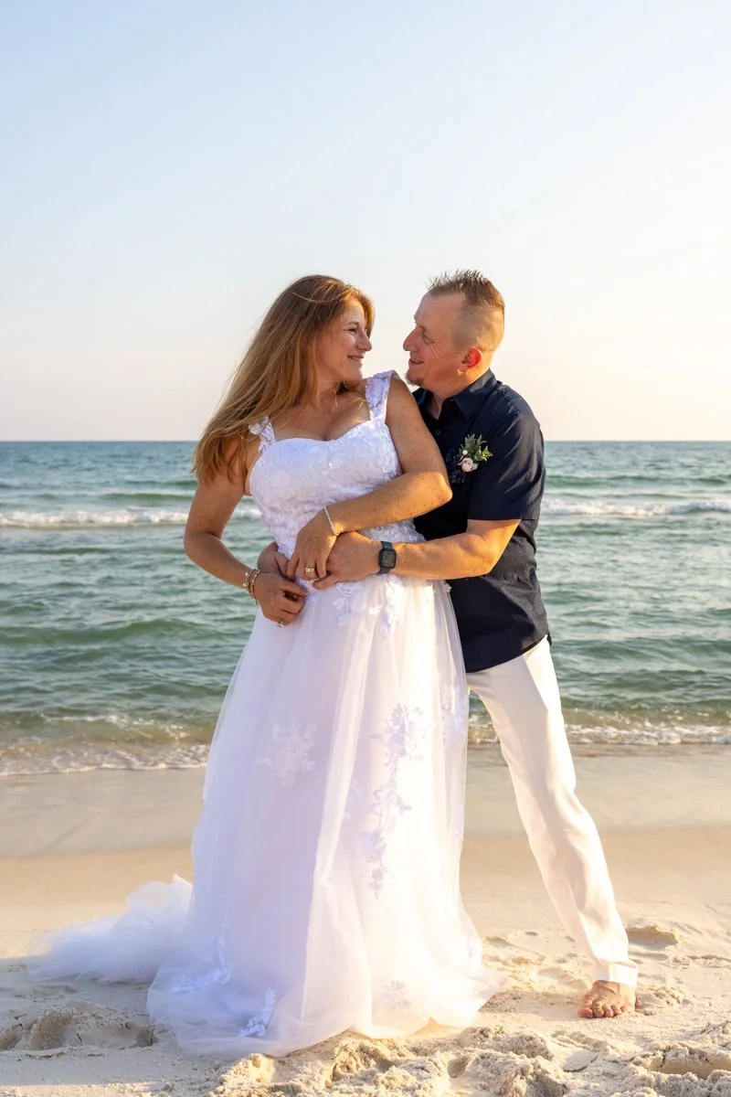 A couple in wedding attire sharing a moment on the beach with the ocean in the background.