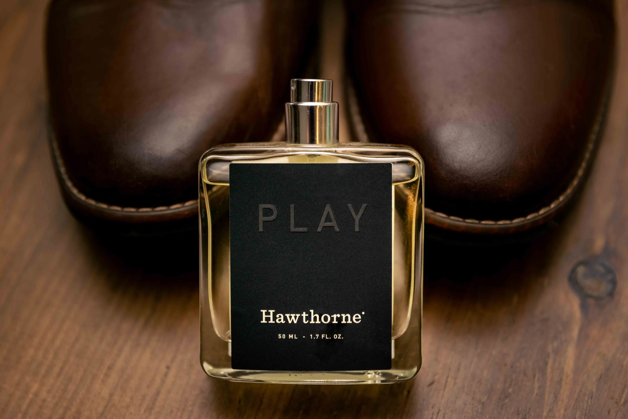A bottle of Hawthorne perfume on a wooden surface with a pair of brown leather shoes in the background.