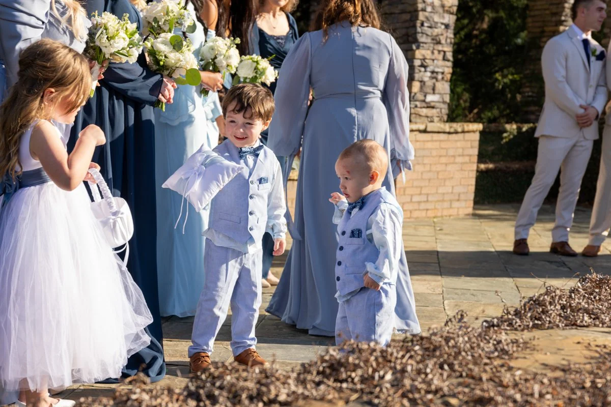 Children dressed in formal clothes at a wedding, with women holding bouquets in the background.