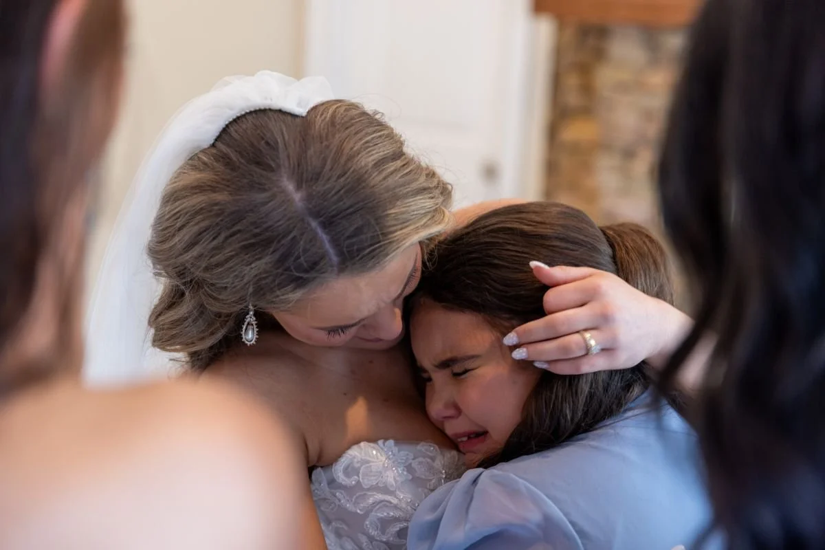 A woman, likely a bride, hugging and comforting a young girl who appears emotional, surrounded by other women.