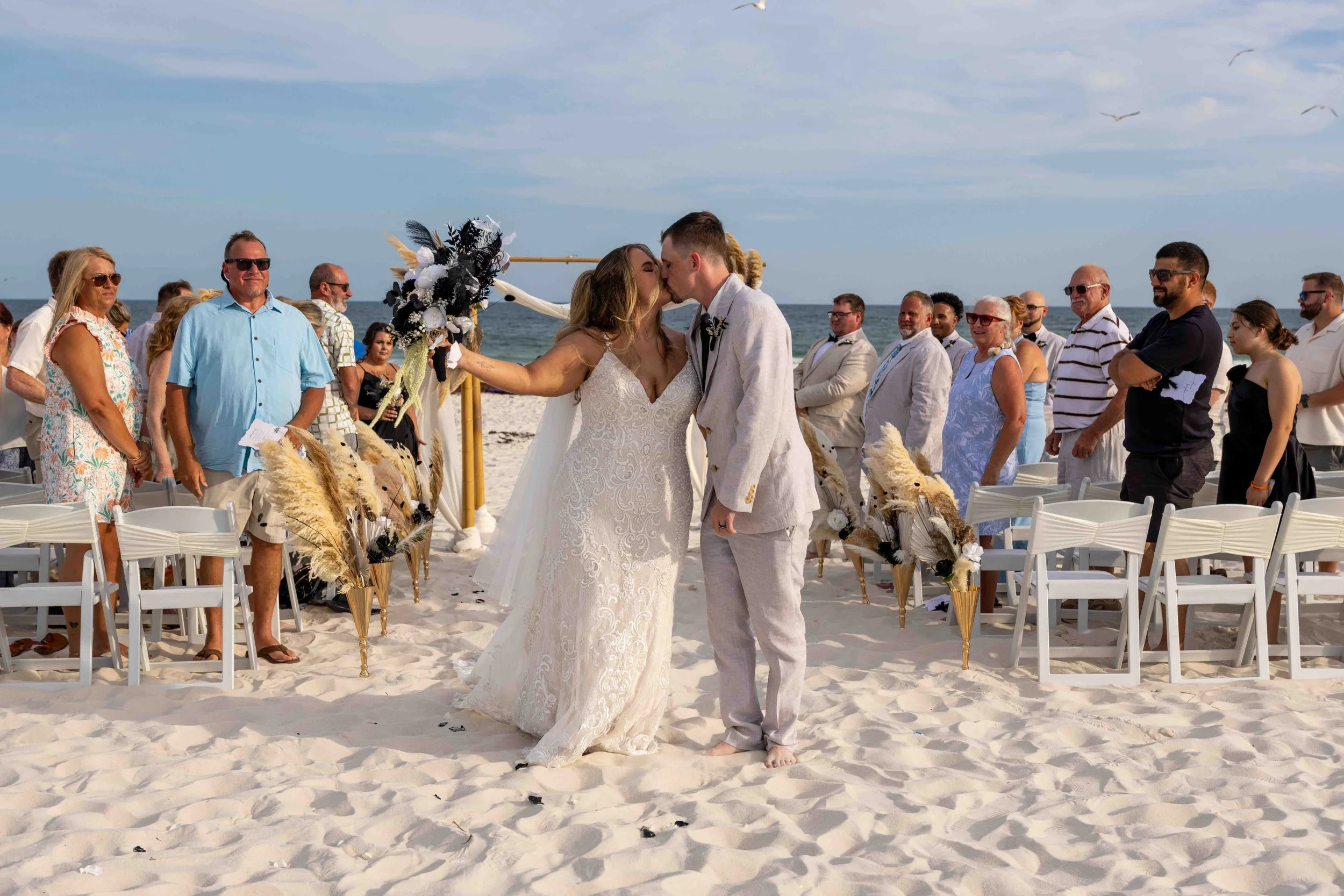 A wedding ceremony on the beach with the bride and groom kissing in front of seated guests and ocean background.