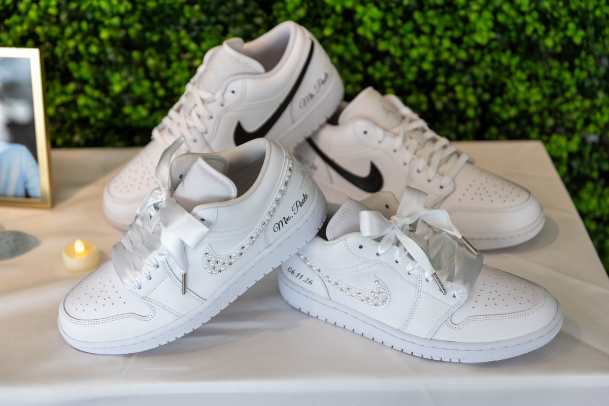 Collection of white sneakers, some with black accents and decorative writing, displayed on a table with a green leafy background.