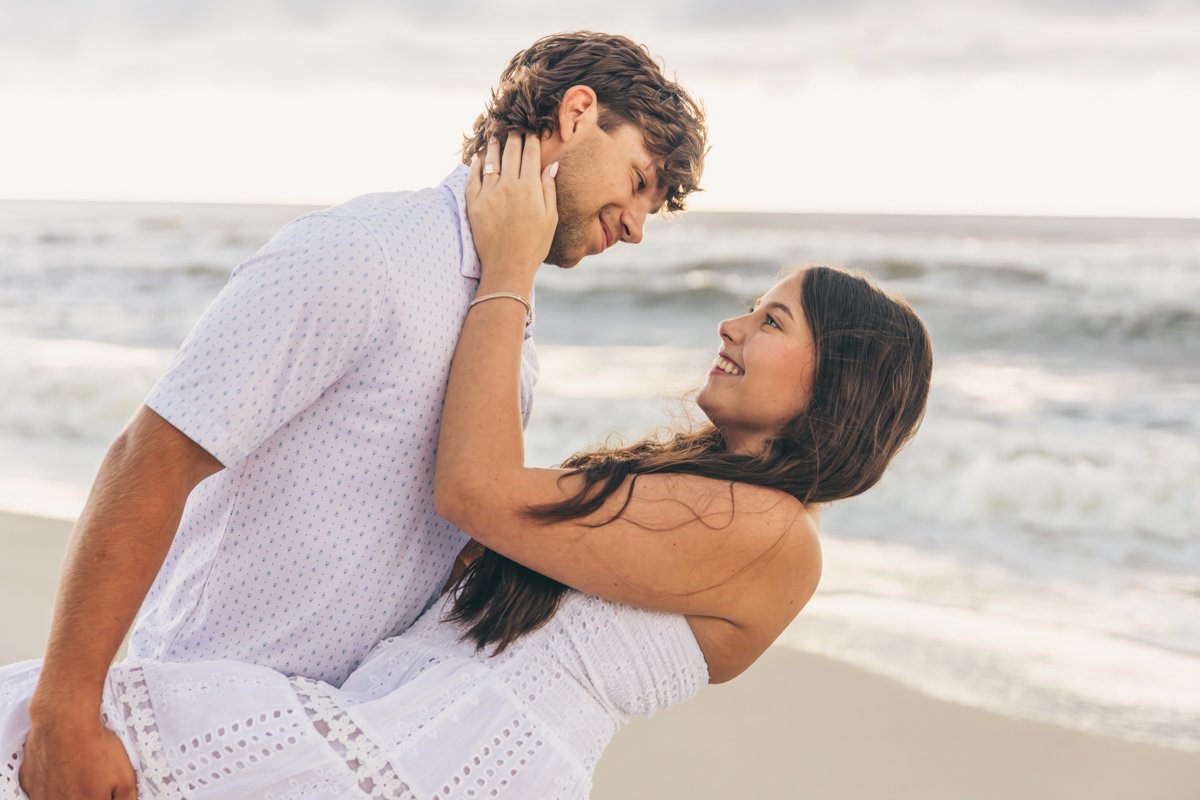 A happy couple embraces on the beach with the ocean in the background.