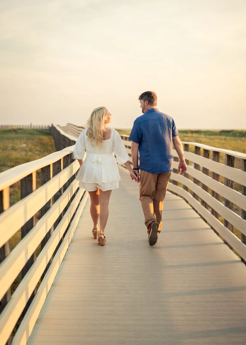 A couple holding hands and walking on a wooden bridge in a natural setting during sunset.