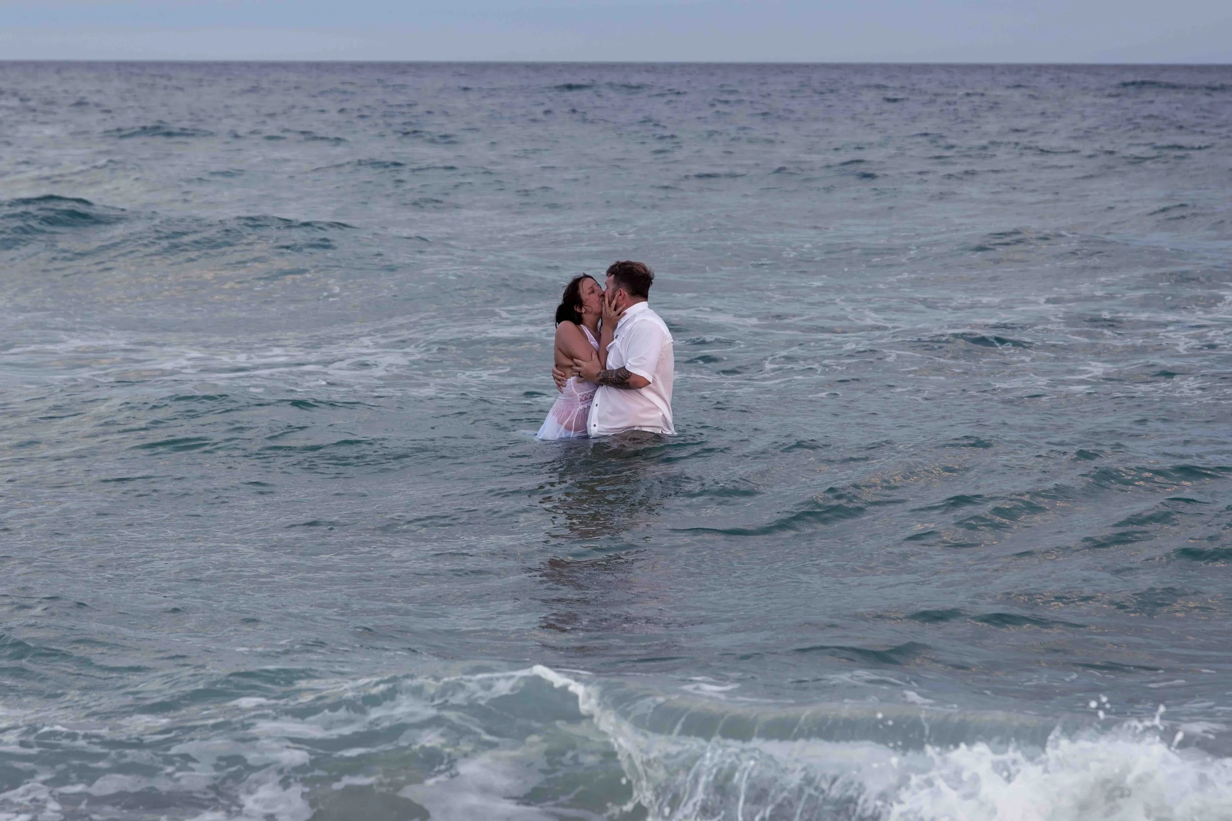 A couple kissing in the ocean with waves around them