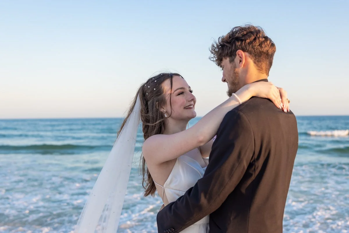 A couple in wedding attire embracing on the beach at sunset