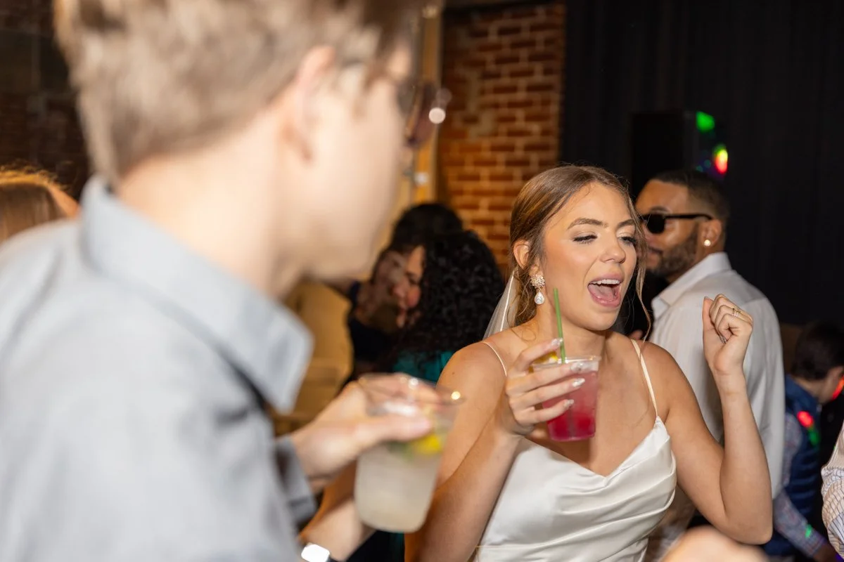 A woman dancing with a drink at a party, with other people in the background.