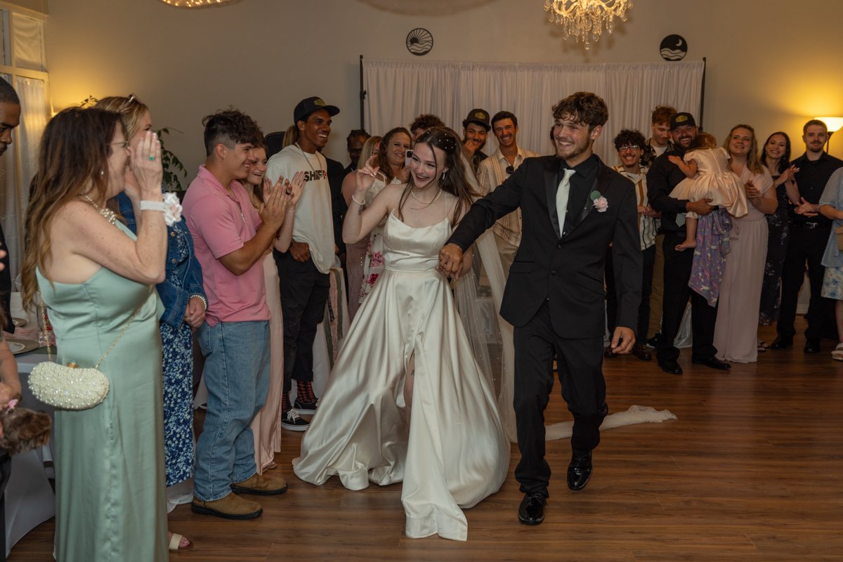 A bride and groom dancing at their wedding reception with guests smiling and clapping around them.