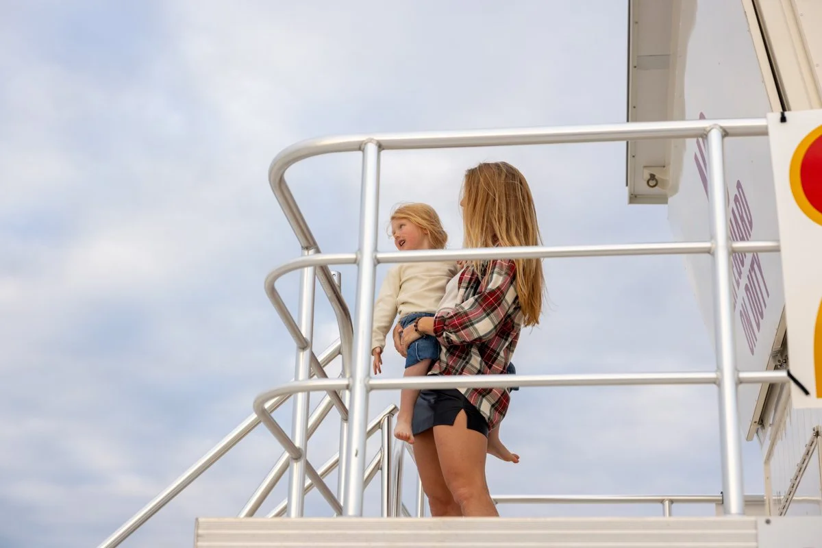 A woman holding a young girl on a carnival ride platform with a cloudy sky in the background.