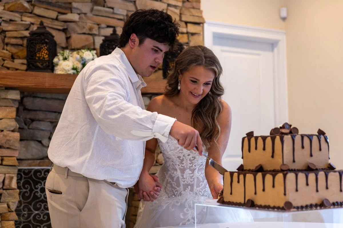 A young couple in wedding attire cutting a wedding cake together at a celebration.
