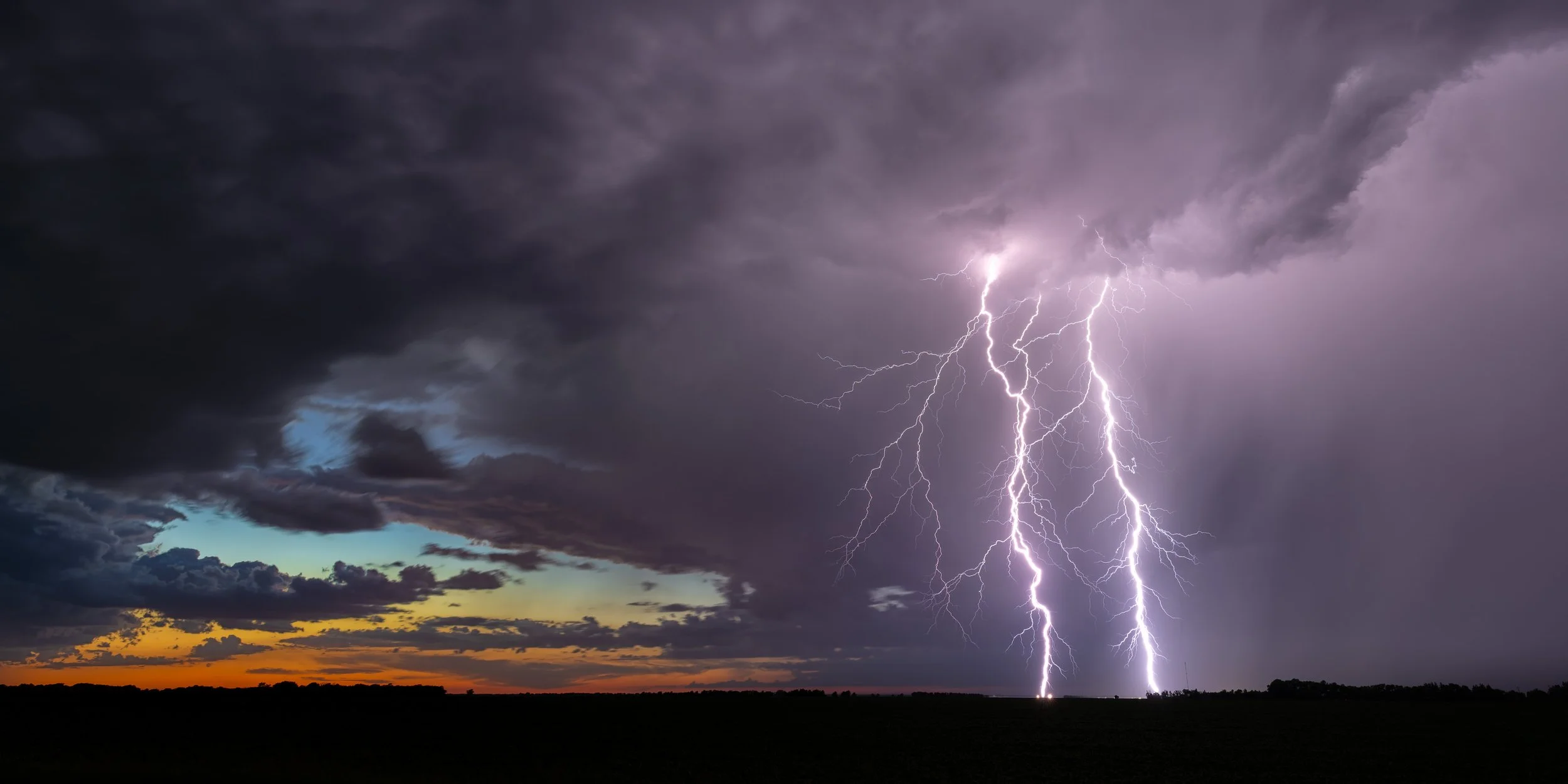 Powerful lightning strike beneath dark storm clouds over the Manitoba prairies at sunset