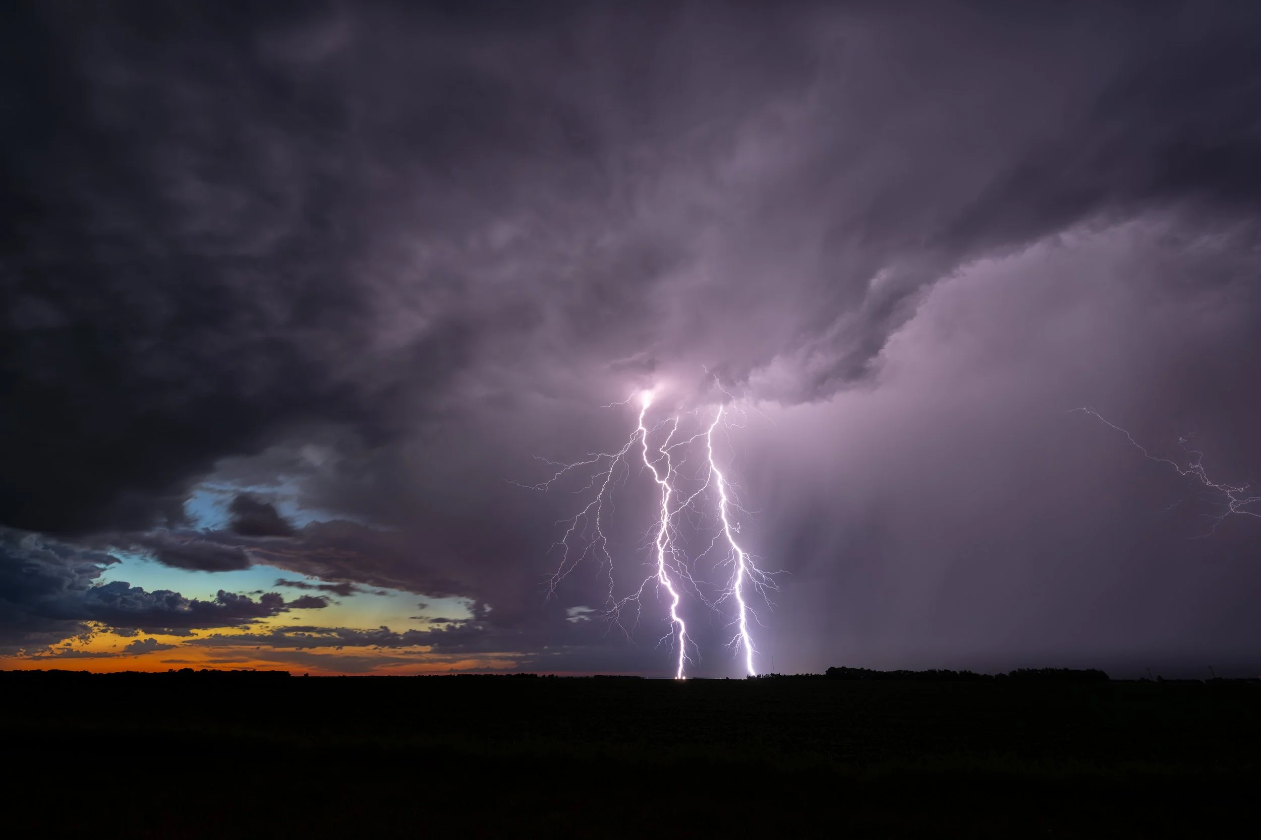 Brilliant lightning illuminating a massive prairie storm beneath the fading evening sky