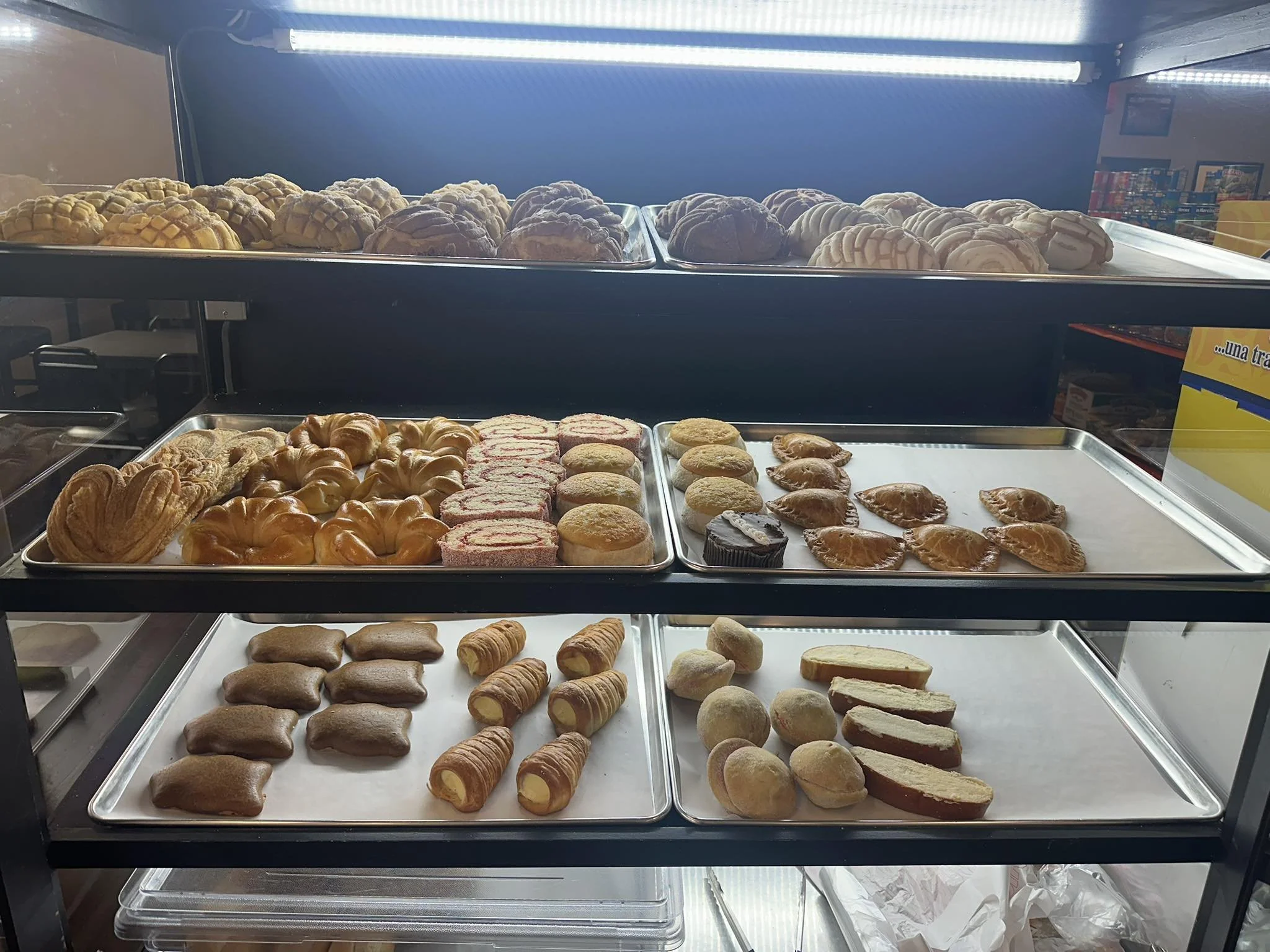 Display case with various baked goods including cookies, croissants, and pastries, illuminated by bright overhead lighting.