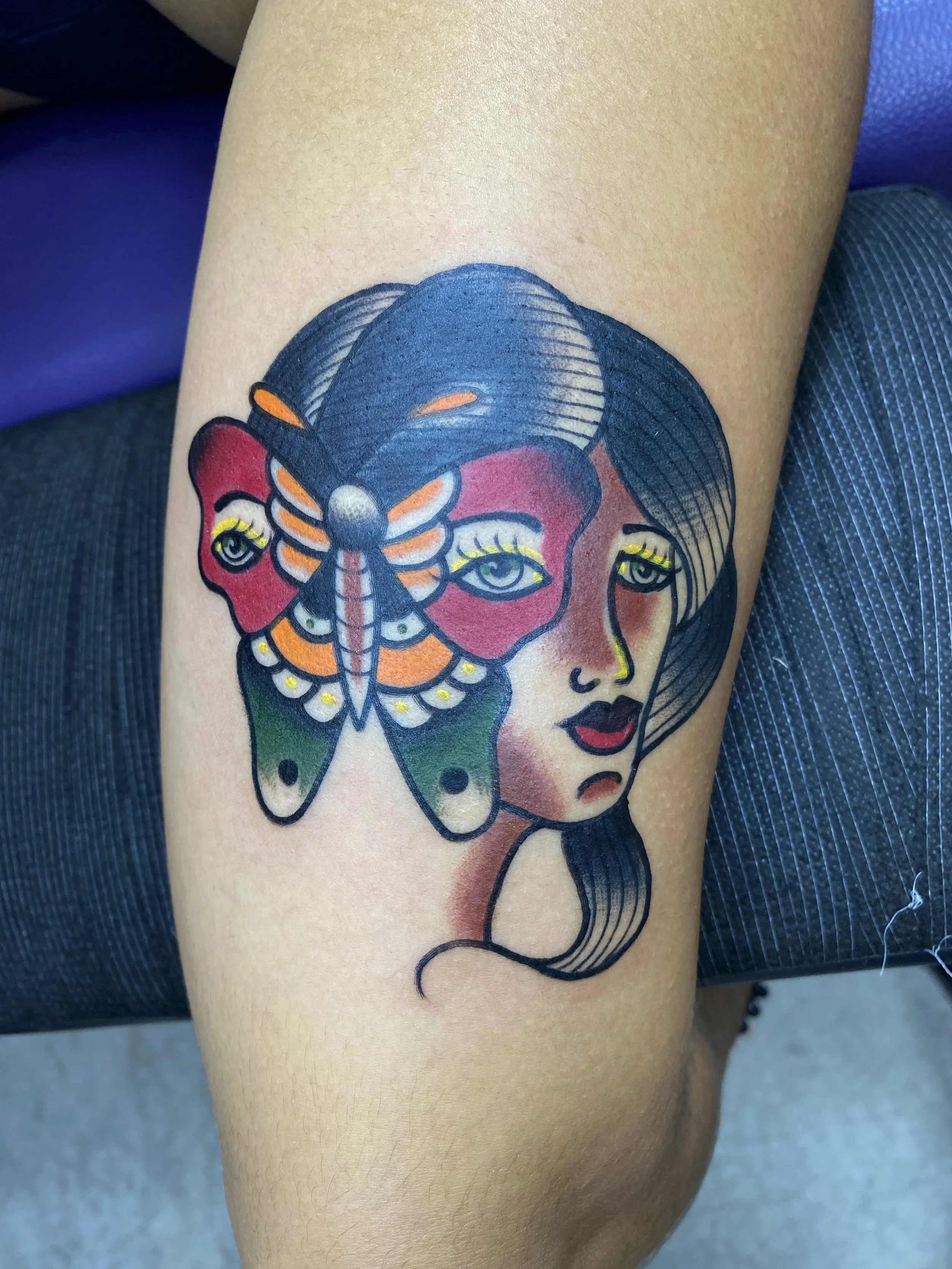 Tattoo of a woman’s face and a colorful butterfly with a black outline on her shoulder.