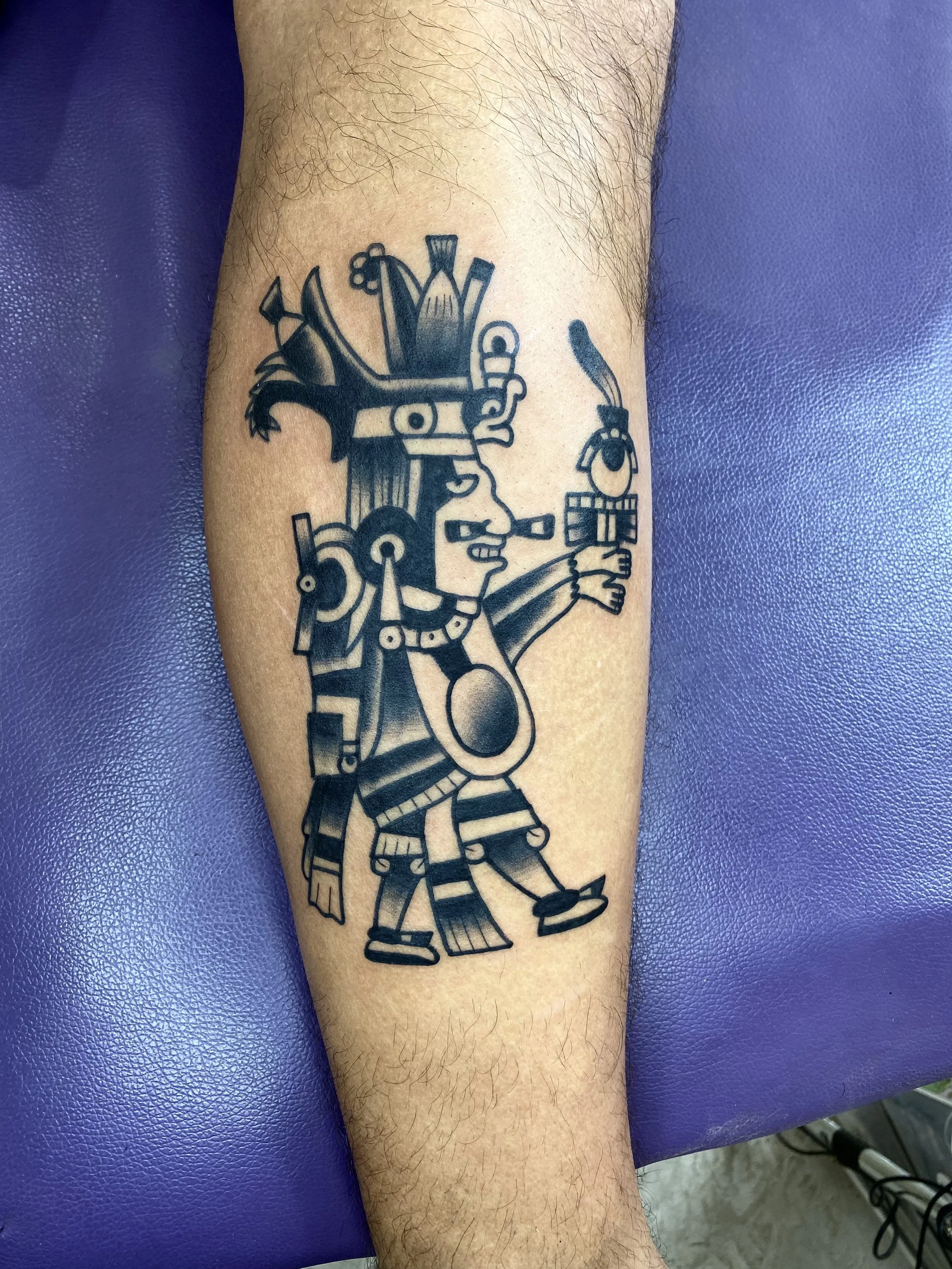 A tattoo of a robot with a humanoid shape, holding a sword, and wearing a helmet with a plume. The robot is colored in black ink and is detailed with mechanical features. The tattoo is on a person's forearm, which has some hair.
