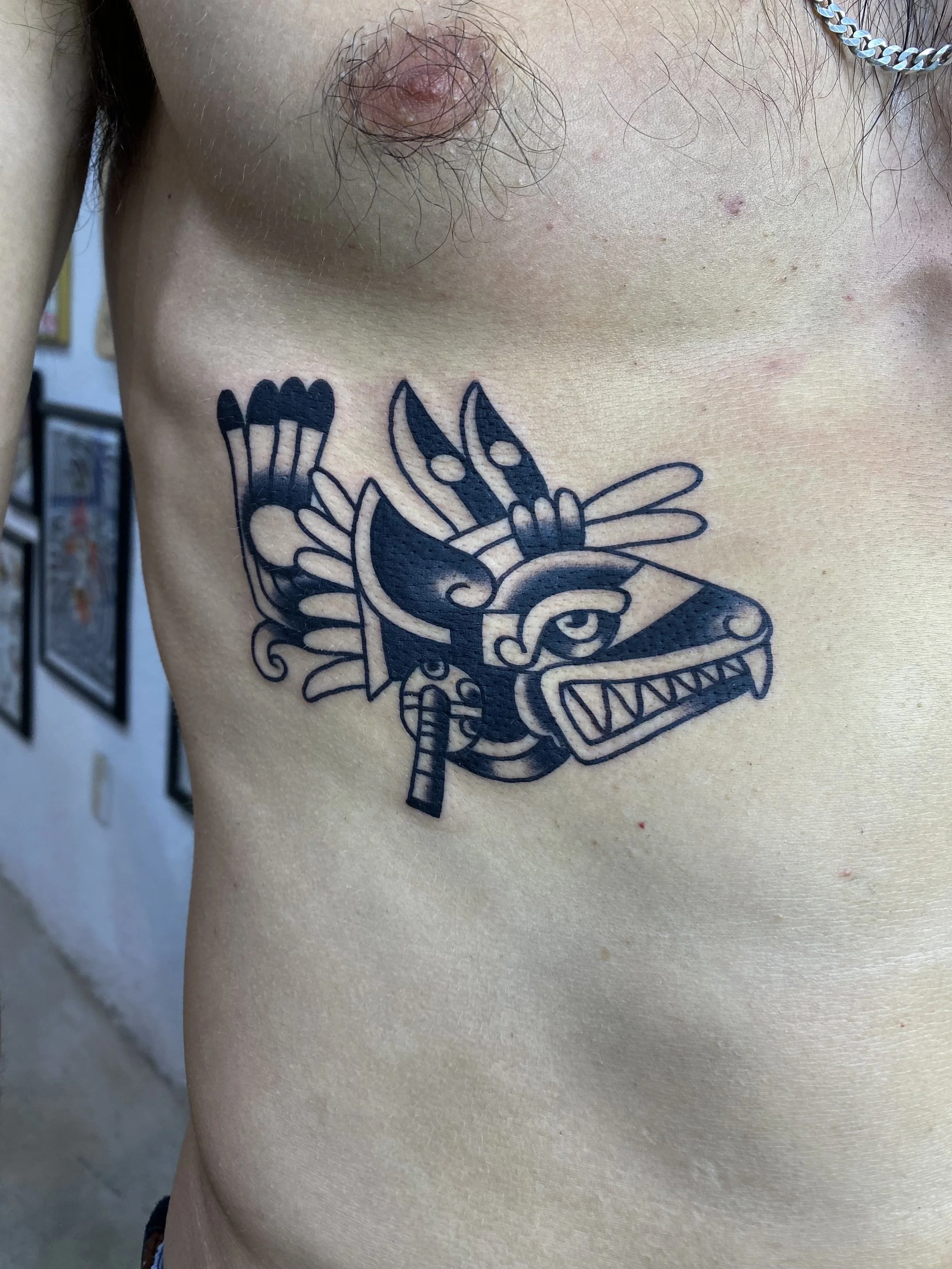 Close-up of a person's upper left chest showing a colorful tattoo of a cartoonish dragon or lizard with sharp teeth and claws.