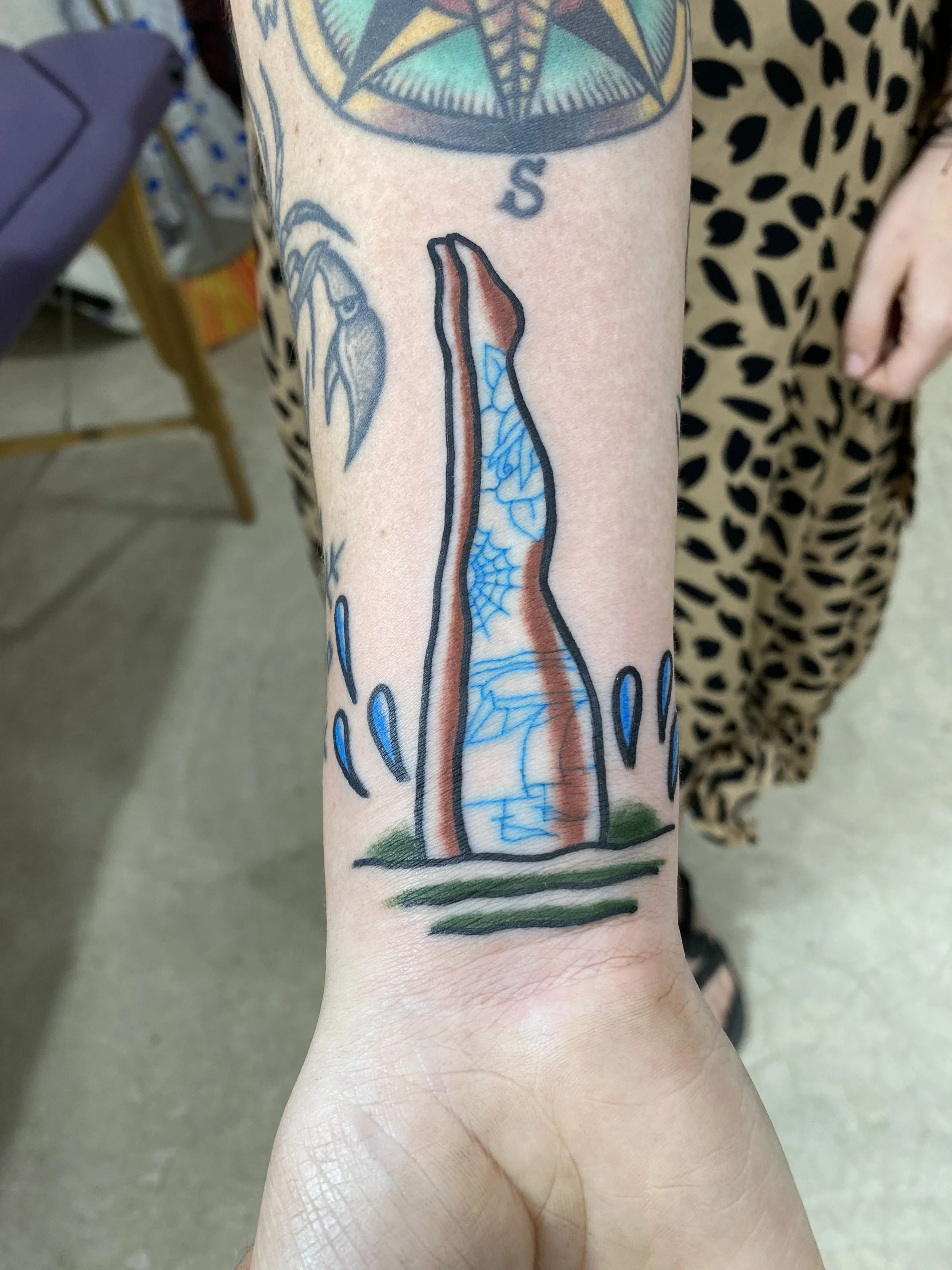 Tattoo of a feminist fist with a barbed wire pattern inside the fist, rising from the ground, with a background circle that looks like a compass or star, on a person's forearm.