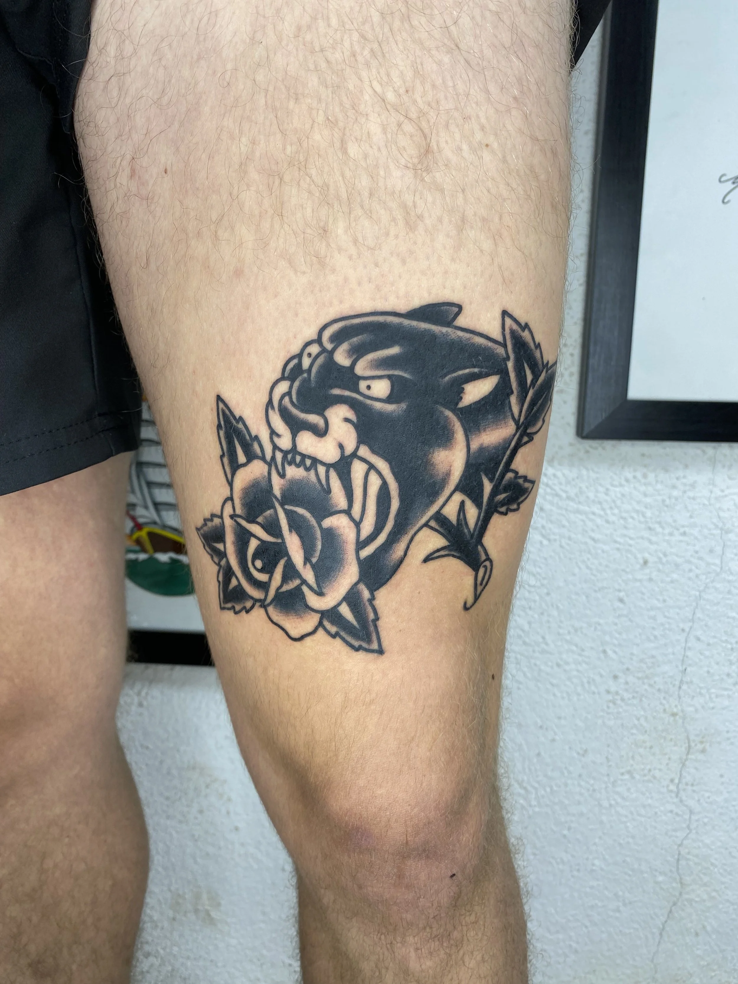 Tattoo of a fierce cartoonish wolf head and rose on person's upper thigh.