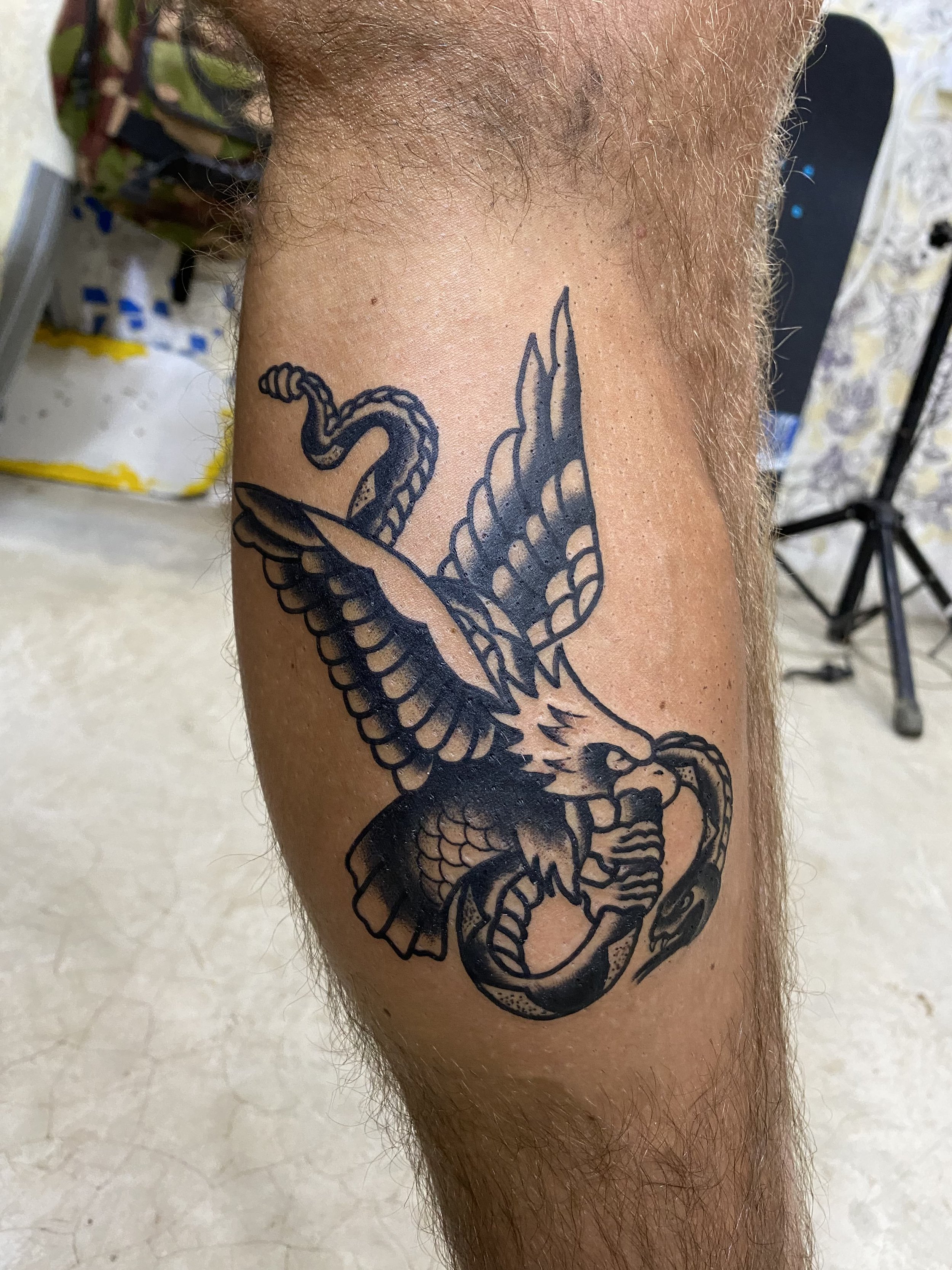 Black and gray tattoo of a dragon on person's forearm with hair nearby, in an indoor setting.