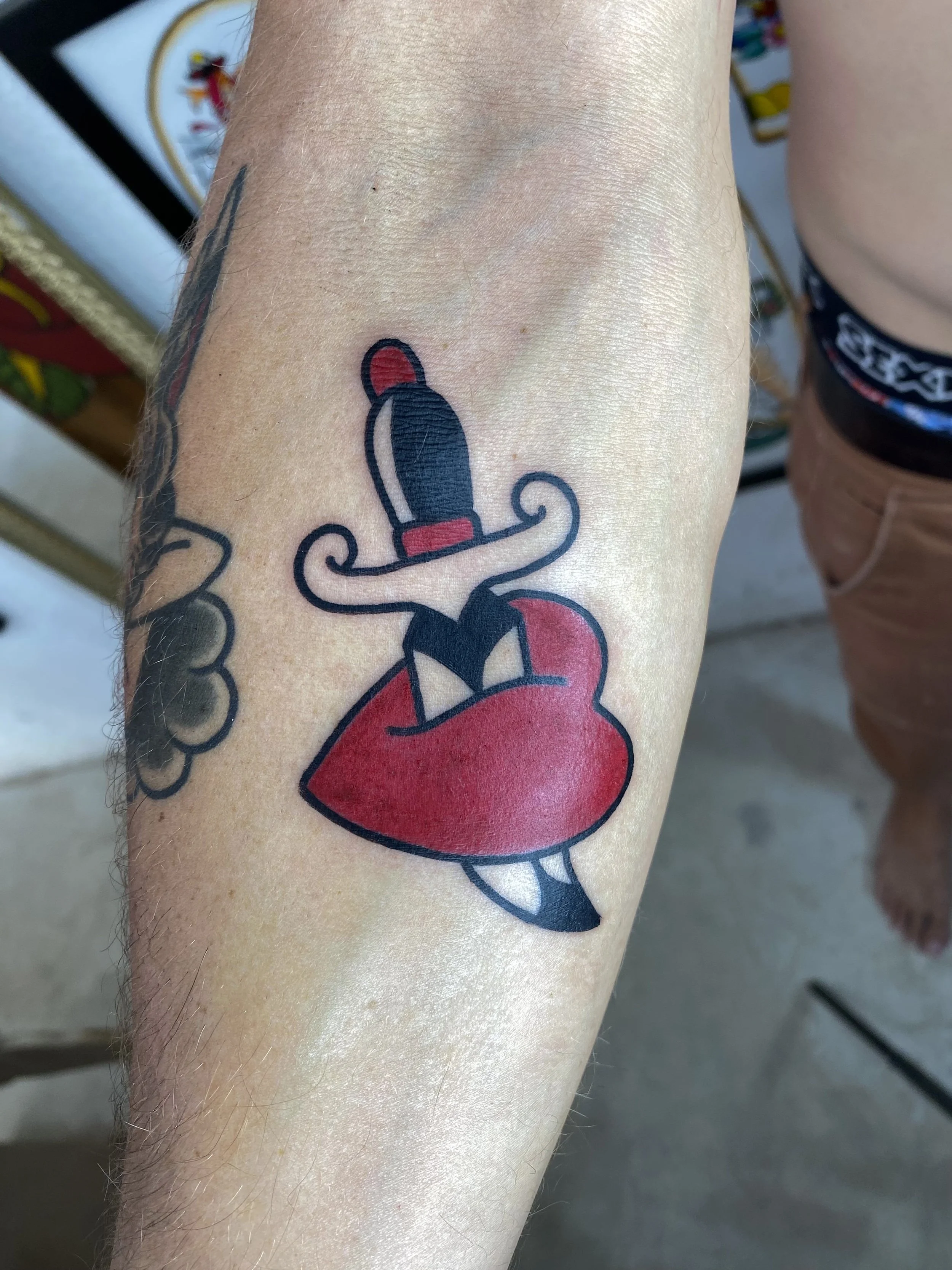 Tattoo of a red heart with a lit cigarette on a person's arm.