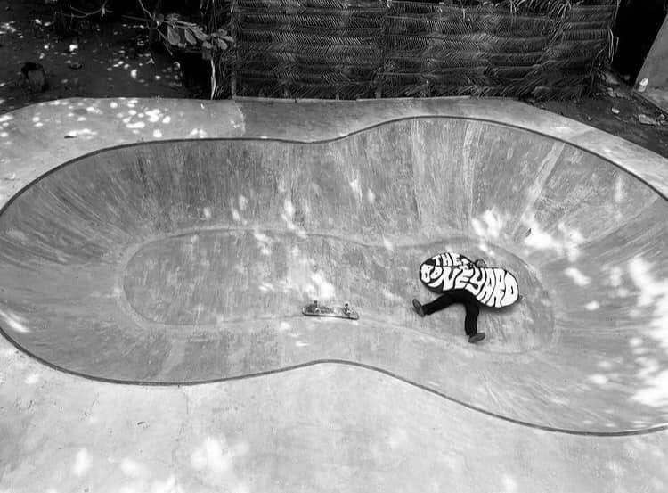 A person in a hoodie with mark arts on it skating in a concrete skate bowl.