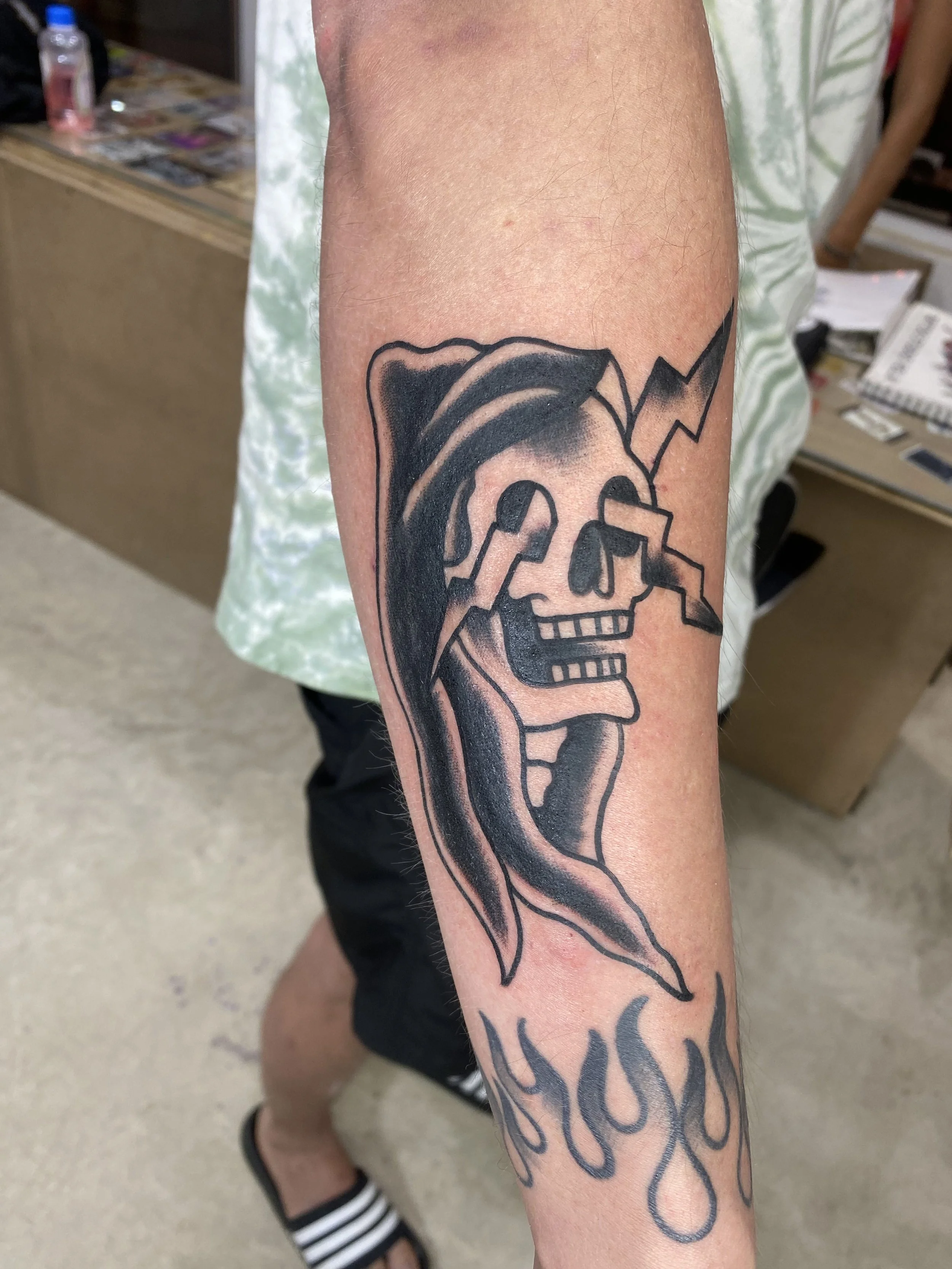 Tattoo of a skull with a hairdo and lightning bolt, and the words 'Stay Trippy' in stylized font on person's arm.