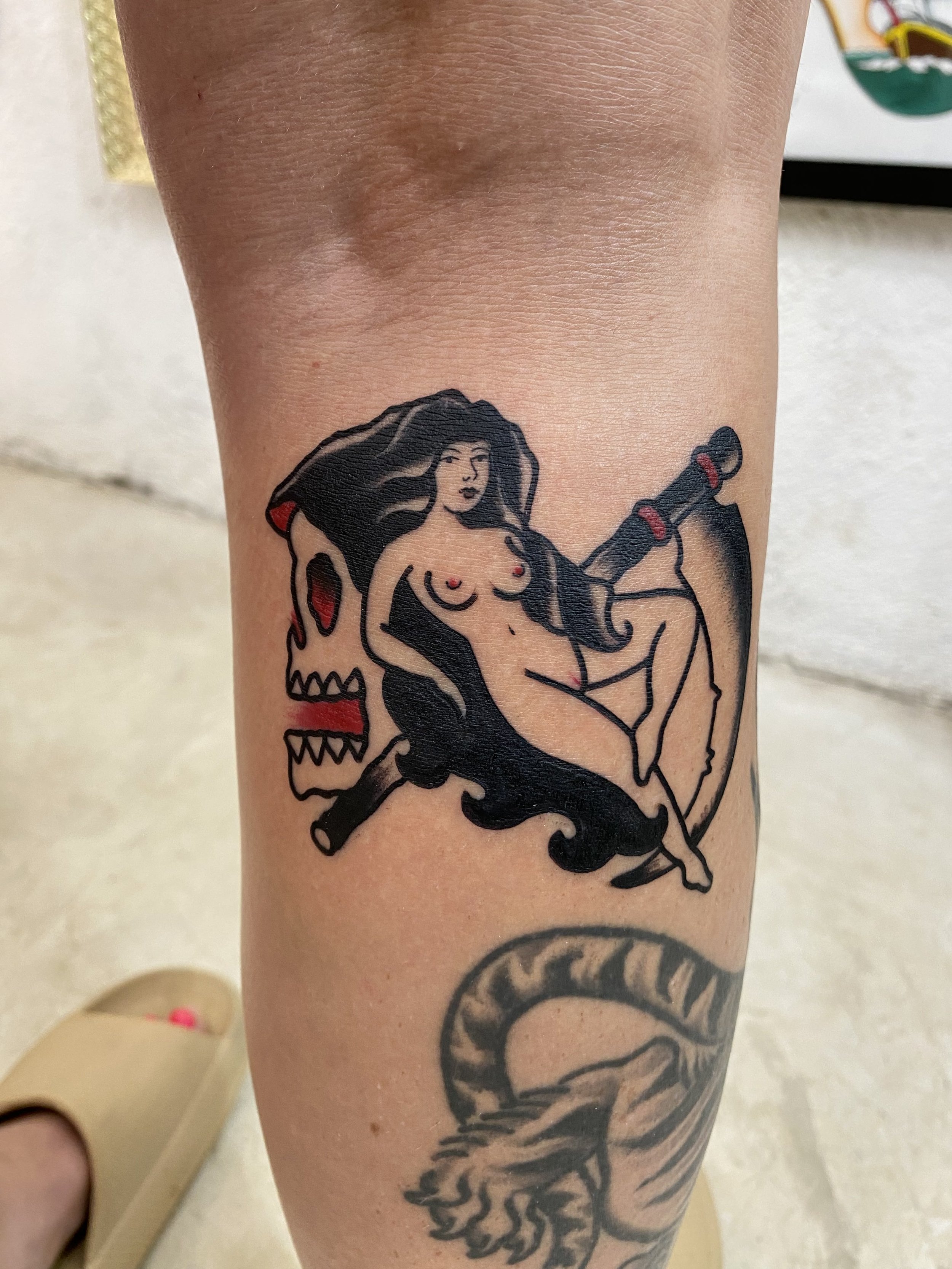 Tattoo of a woman with long hair and a snake on her leg.
