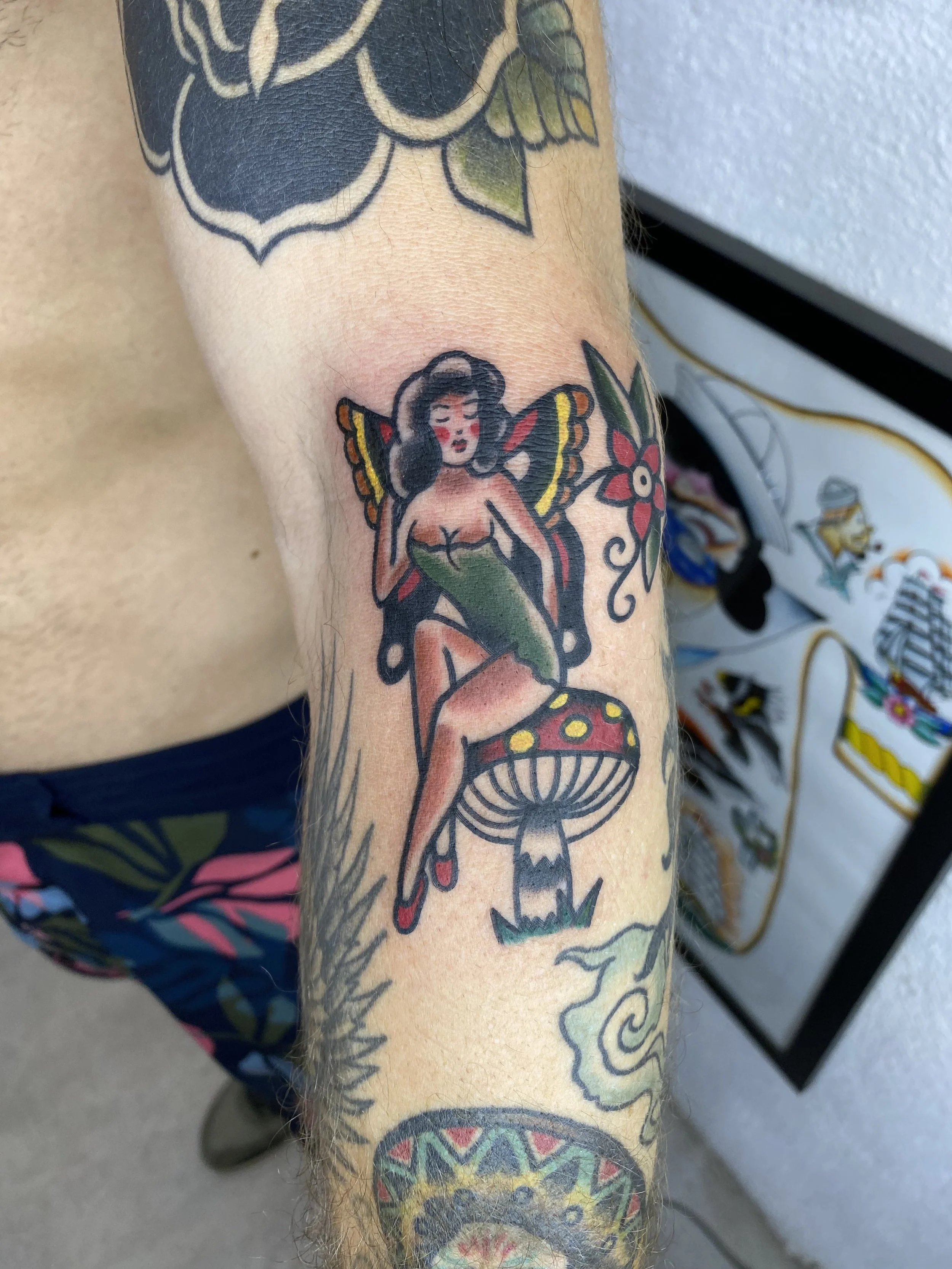 Tattoo on person's arm depicting a woman with butterfly wings, floral elements, and decorative patterns in bold black outline and vibrant colors.