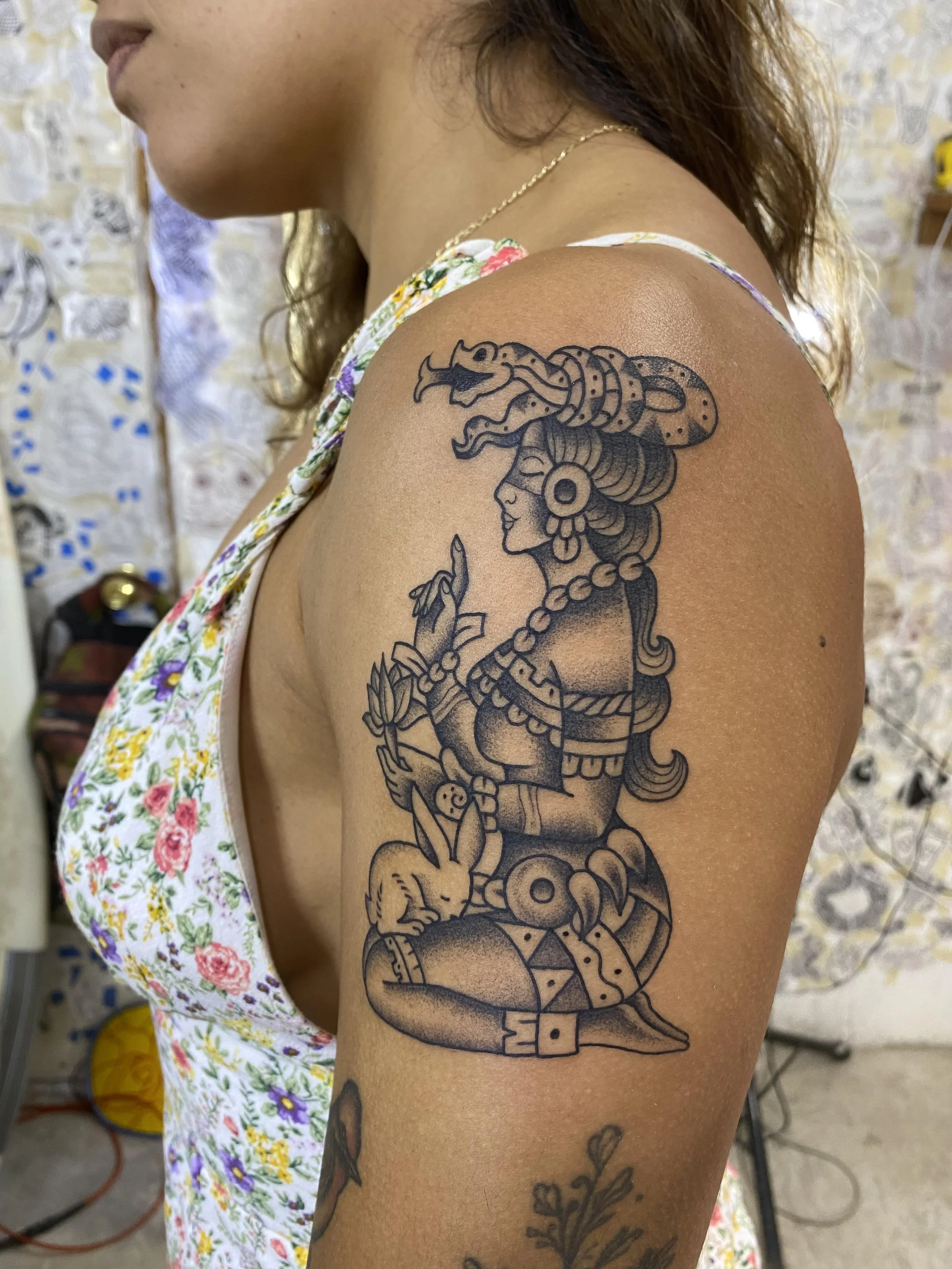 Tattoo of a woman with a headdress, snakes, and a rabbit on a person's upper arm.