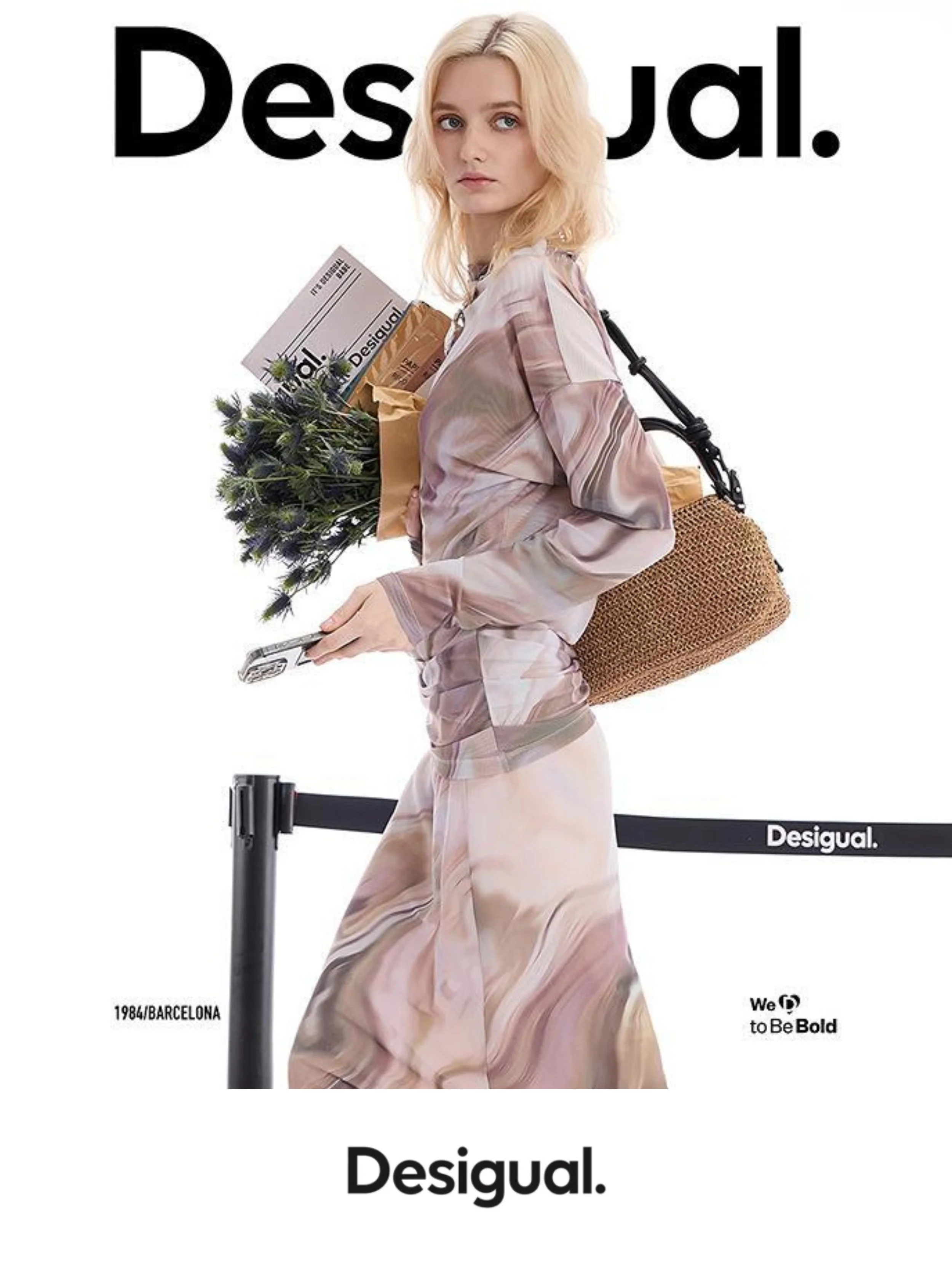 A woman wearing a matching marble-patterned outfit, holding a bouquet of flowers and a newspaper. Her shoulder bag is made of woven material. The background features the brand name 'Desigual' with the phrase 'We go to Be Bold' and mentions Barcelona 1984.